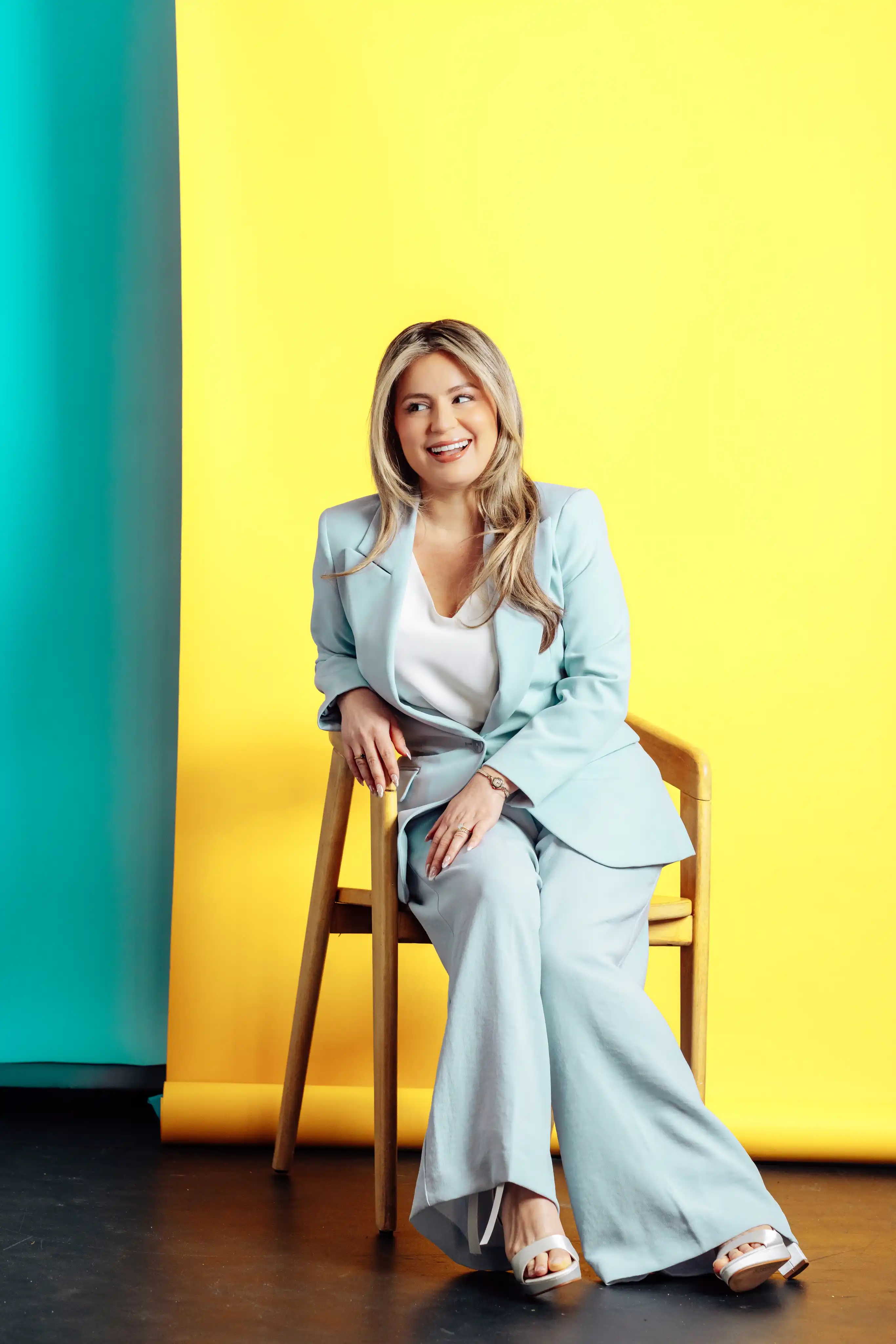 Confident seated business woman wearing light blue suit on yellow and teal background Playful personality portrait against teal backdrop wearing pink blazer for a Tampa branding session in Tampa