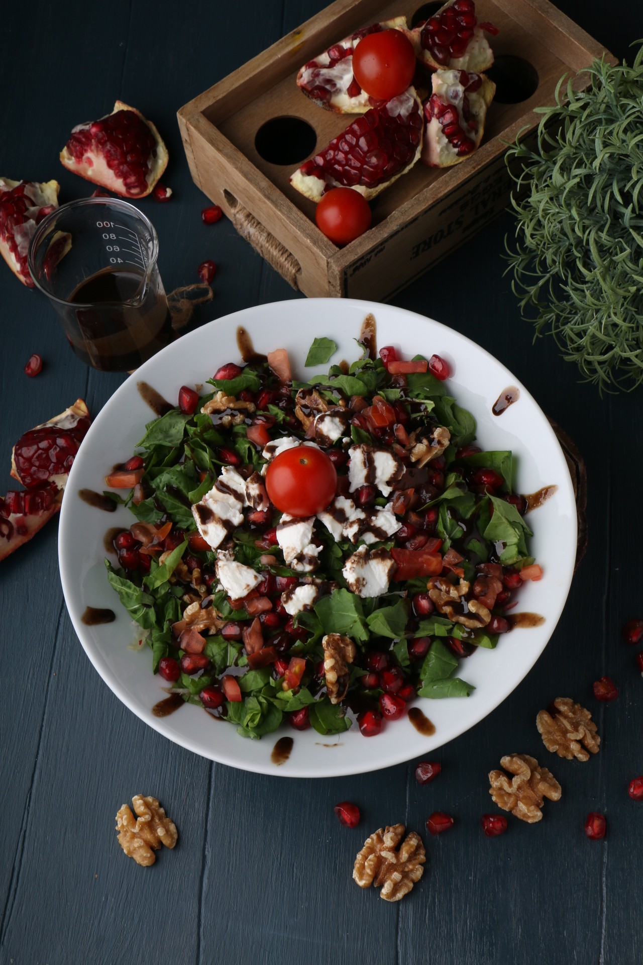 A close-up of a dark gray bowl filled with white fish chunks, cherry tomatoes, green olives, and herbs, served next to a glass of white wine on a white table by a window.