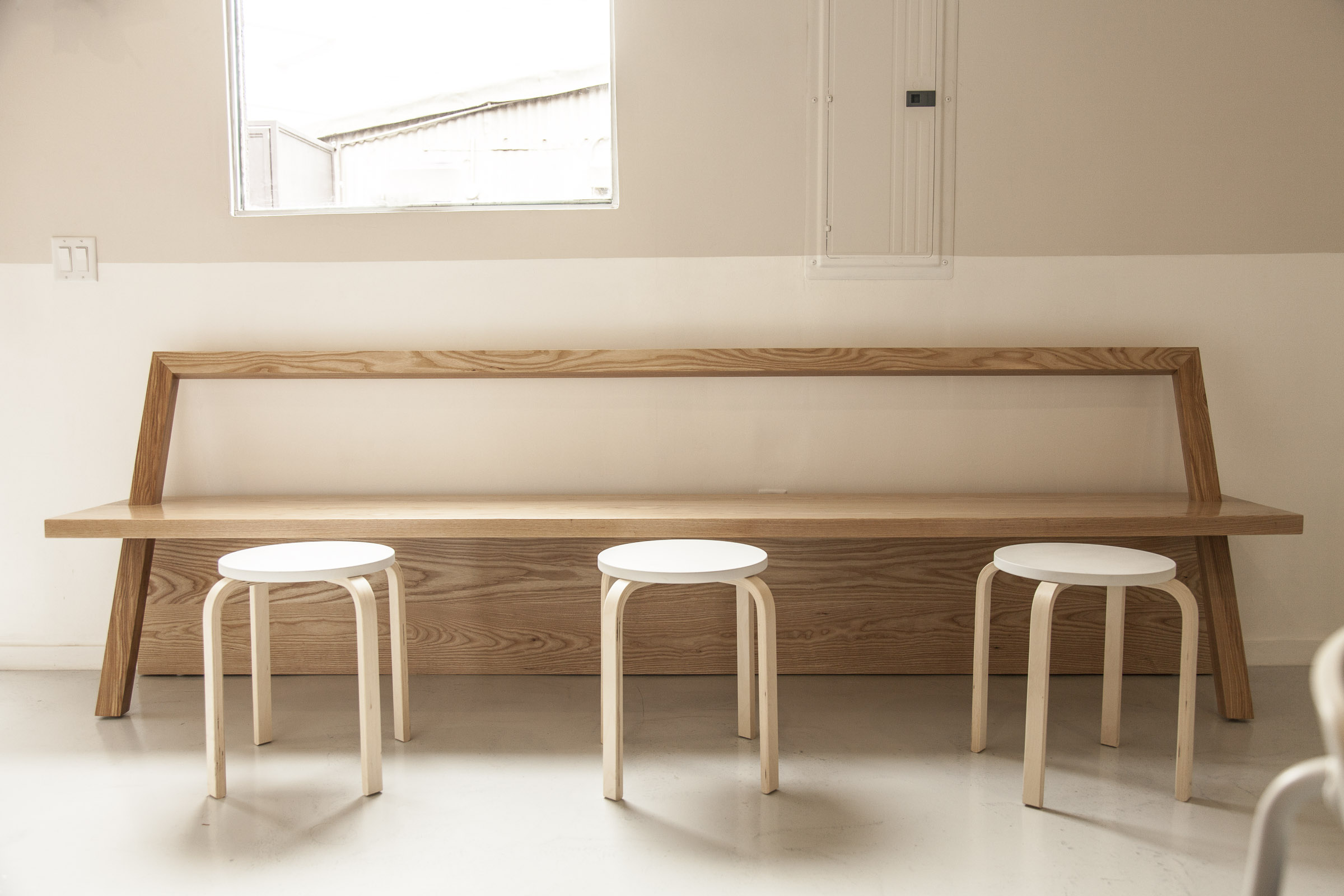 Custom timber bench with three white stools beneath a high window at The Assembly.