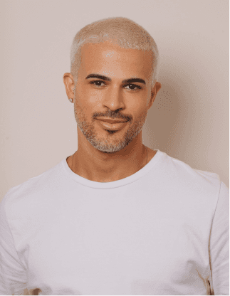 Retrato de um homem com cabelo curto platinado e barba por fazer, vestindo camiseta branca em fundo claro