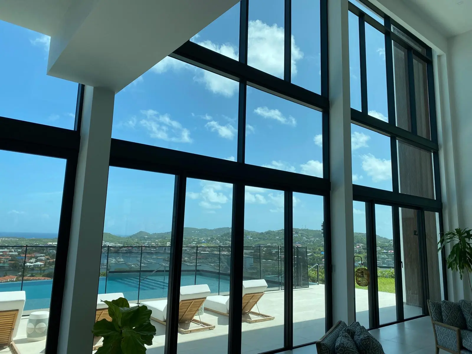 Two-story window wall at The Hill Residence in St. Lucia by Atelier International, looking out to loungers, the infinity pool, and the marina below.