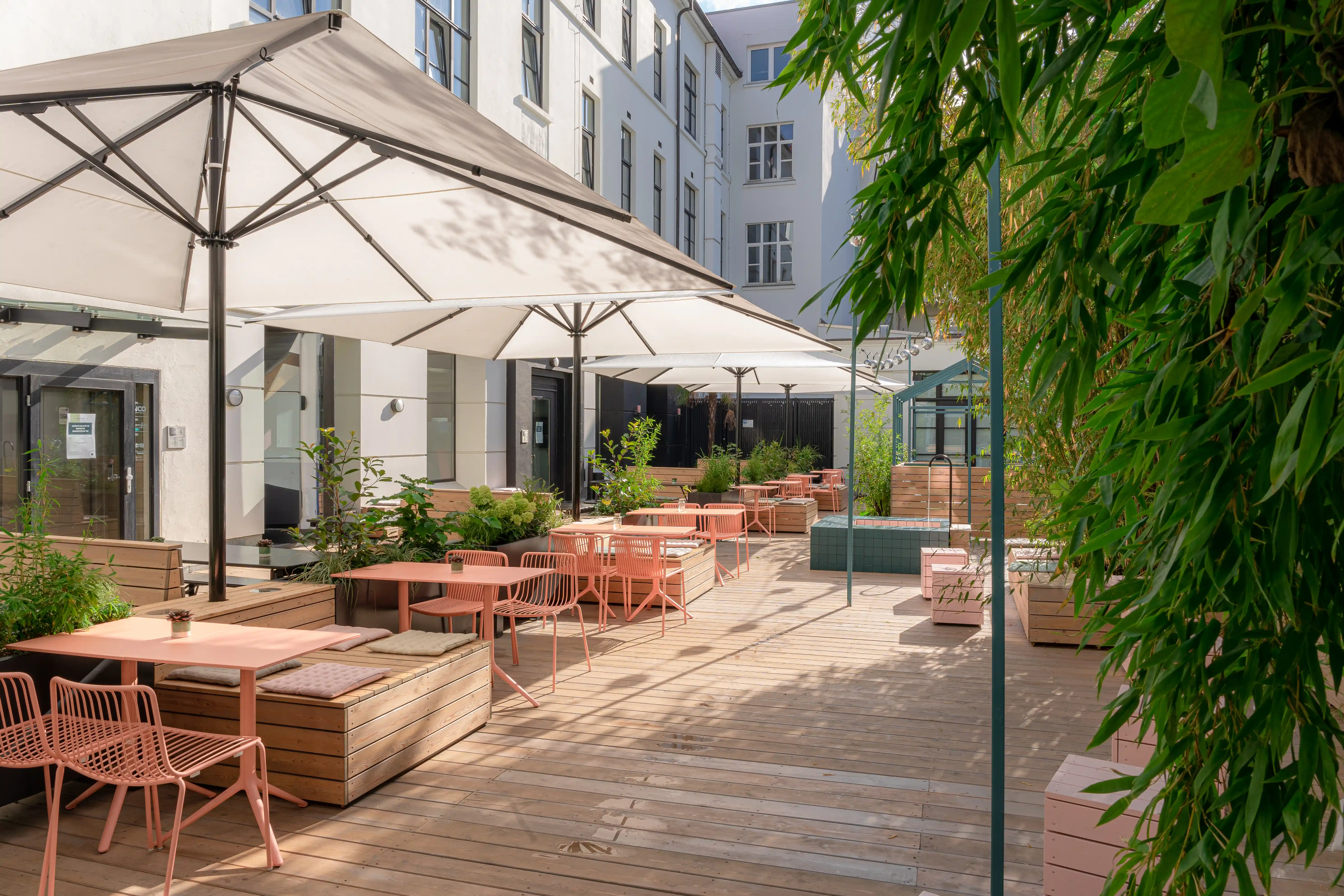 Courtyard terrace at LOKAL VIER with teal house-shaped steel frames, wooden planters with bamboo, decked flooring and white parasols.