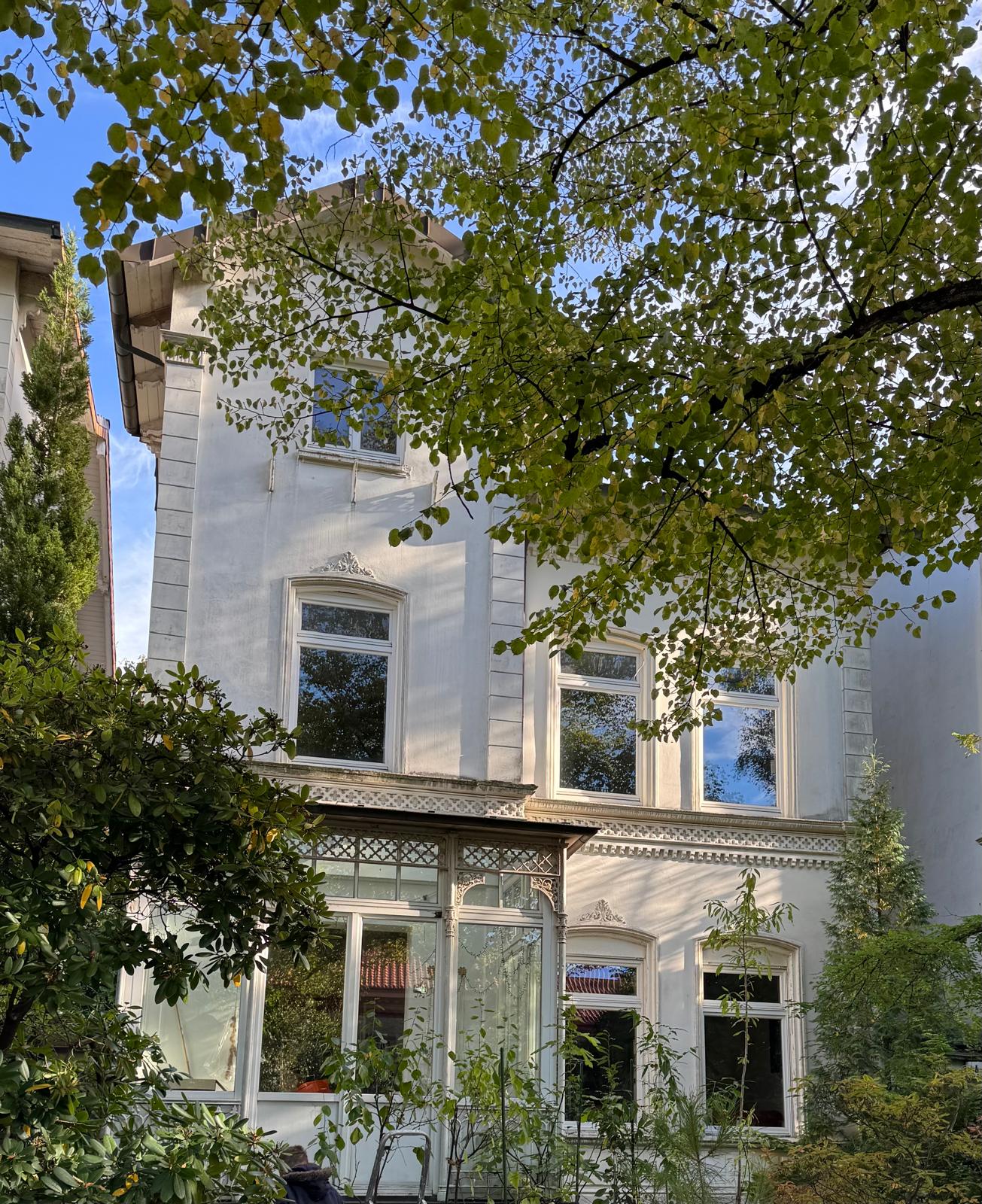 Smiling young man with short hair poses against a dark background, wearing a green button-up shirt.