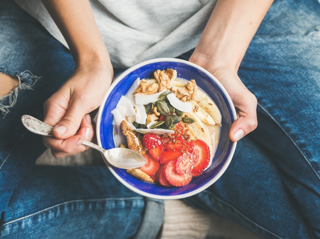 woman eating a healthy breakfast bowl of fruit and granola, showing how to lose weight naturally without exercise