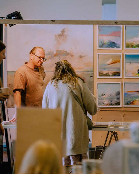 Zdjęcie przedstawiające artyste sprzedającego obraz na stoisku targowym.