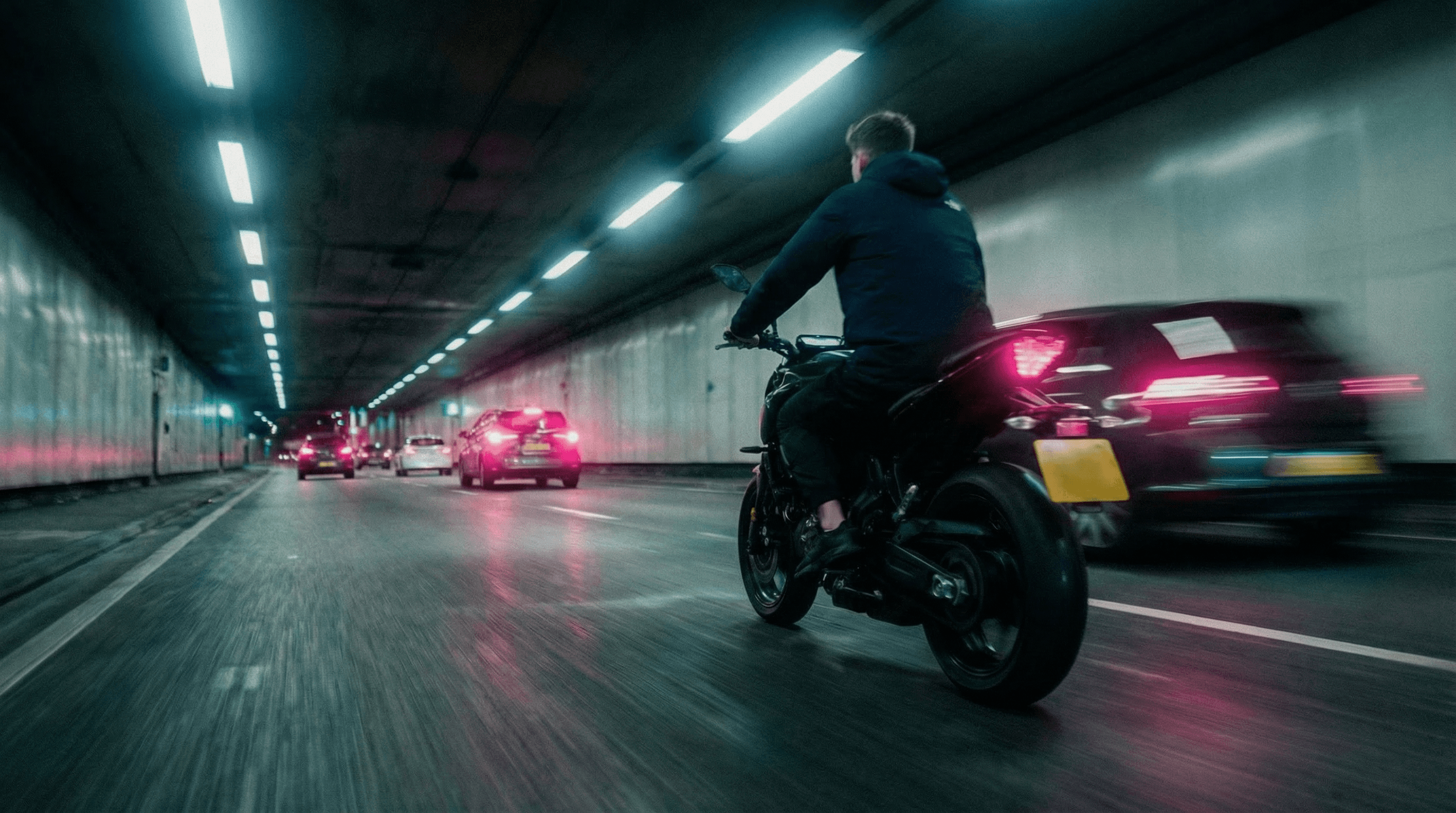 A man in a brown blazer and a woman in a light sweater sit at a desk with a laptop, discussing something. The room is dimly lit, creating a focused atmosphere.