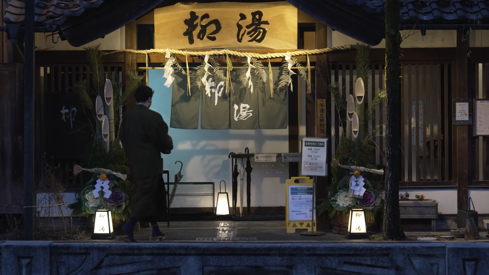A bather in yukata stepping through the noren into Yanagi-yu bathhouse in Kinosaki.