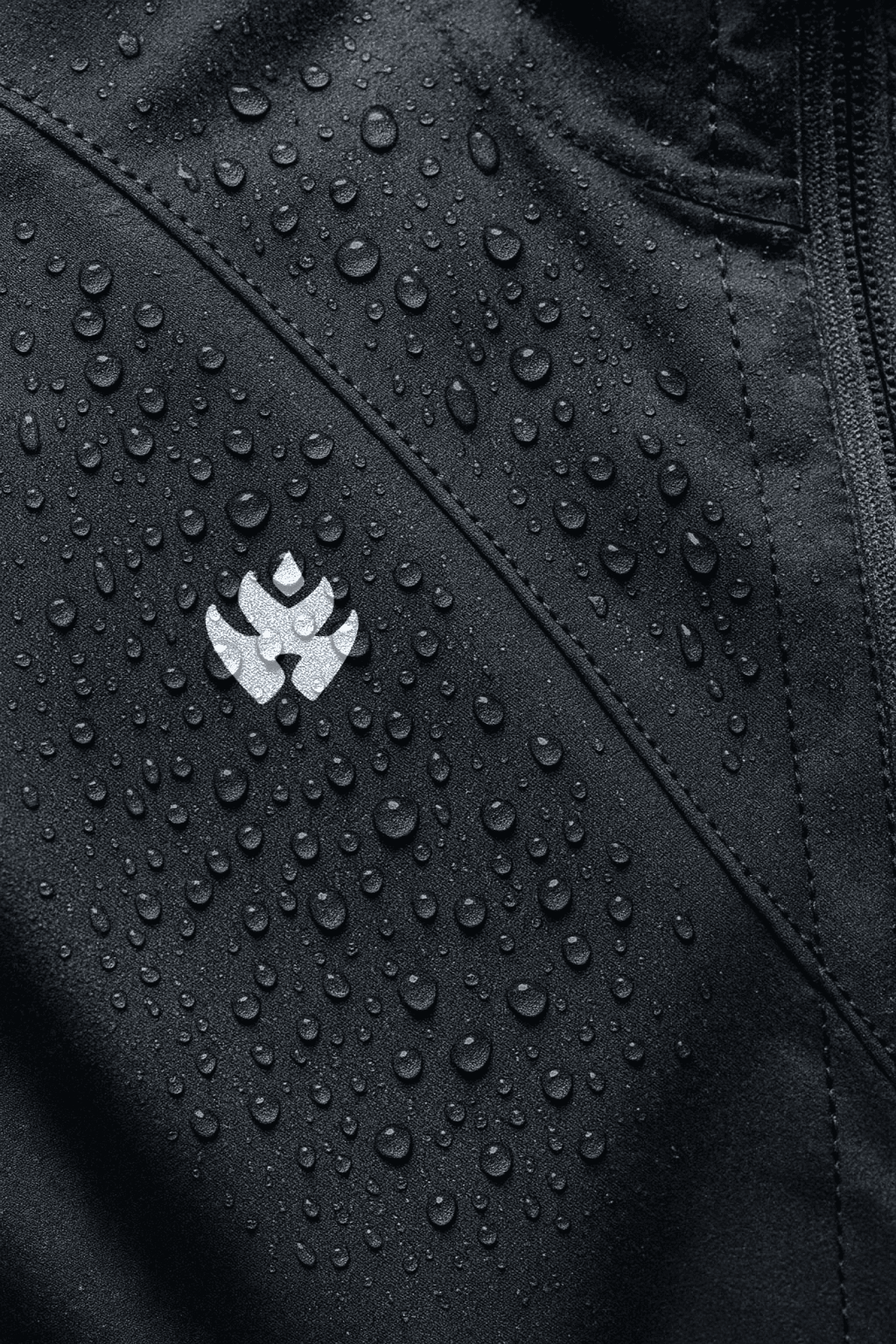 Close-up of a black waterproof jacket with water droplets on the surface and a small reflective logo.