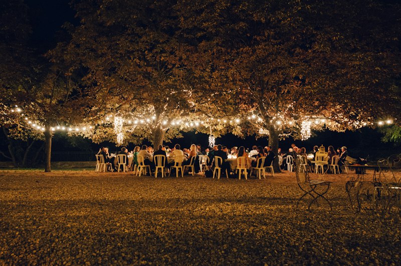 Guests at long tables beneath trees strung with warm lights at a welcome dinner