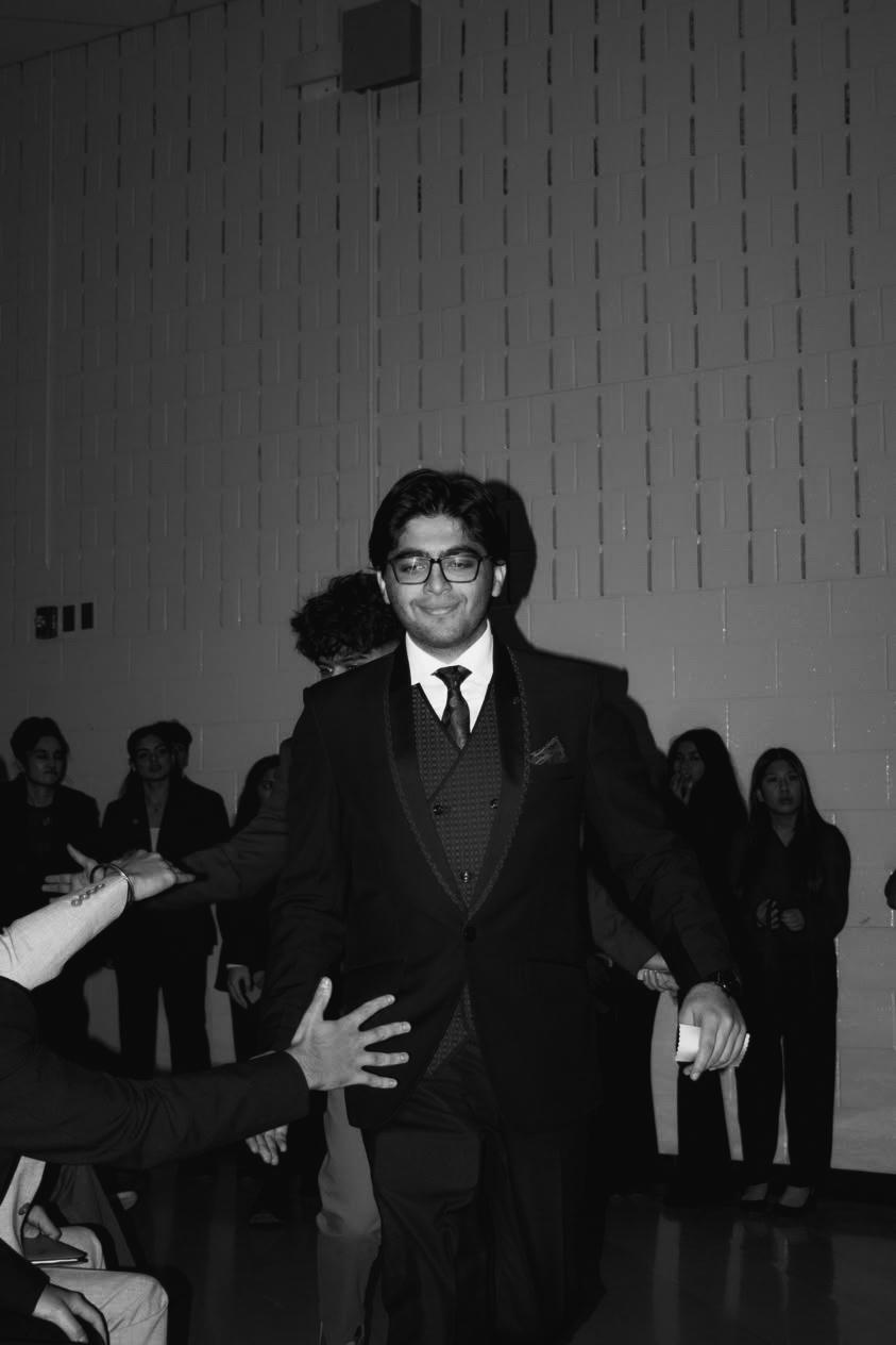 A confident person with short, styled hair and a leather jacket poses against a dark backdrop.