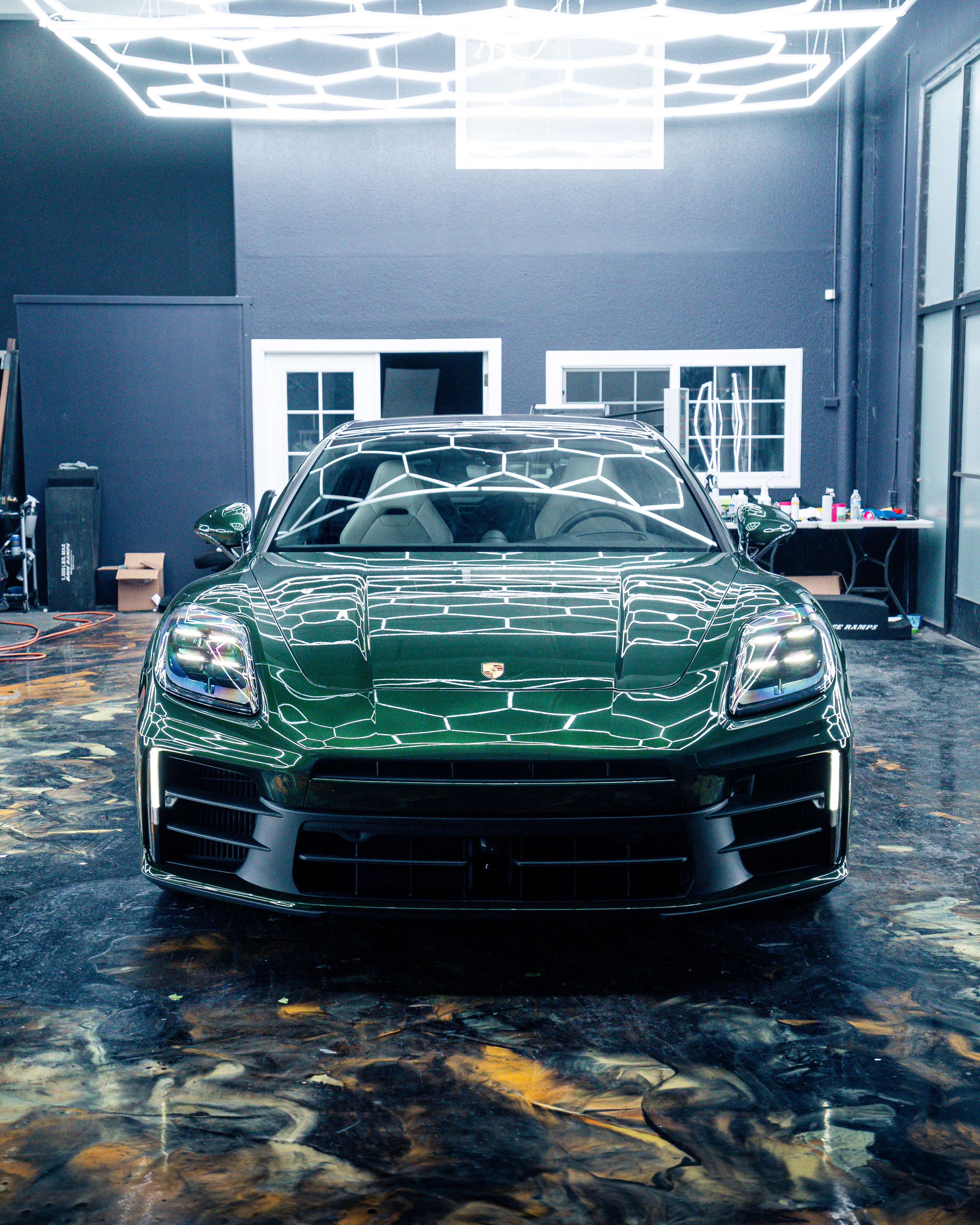 Front-facing British Racing Green Porsche Panamera at Dragon Auto Milpitas with hexagon ceiling lights overhead