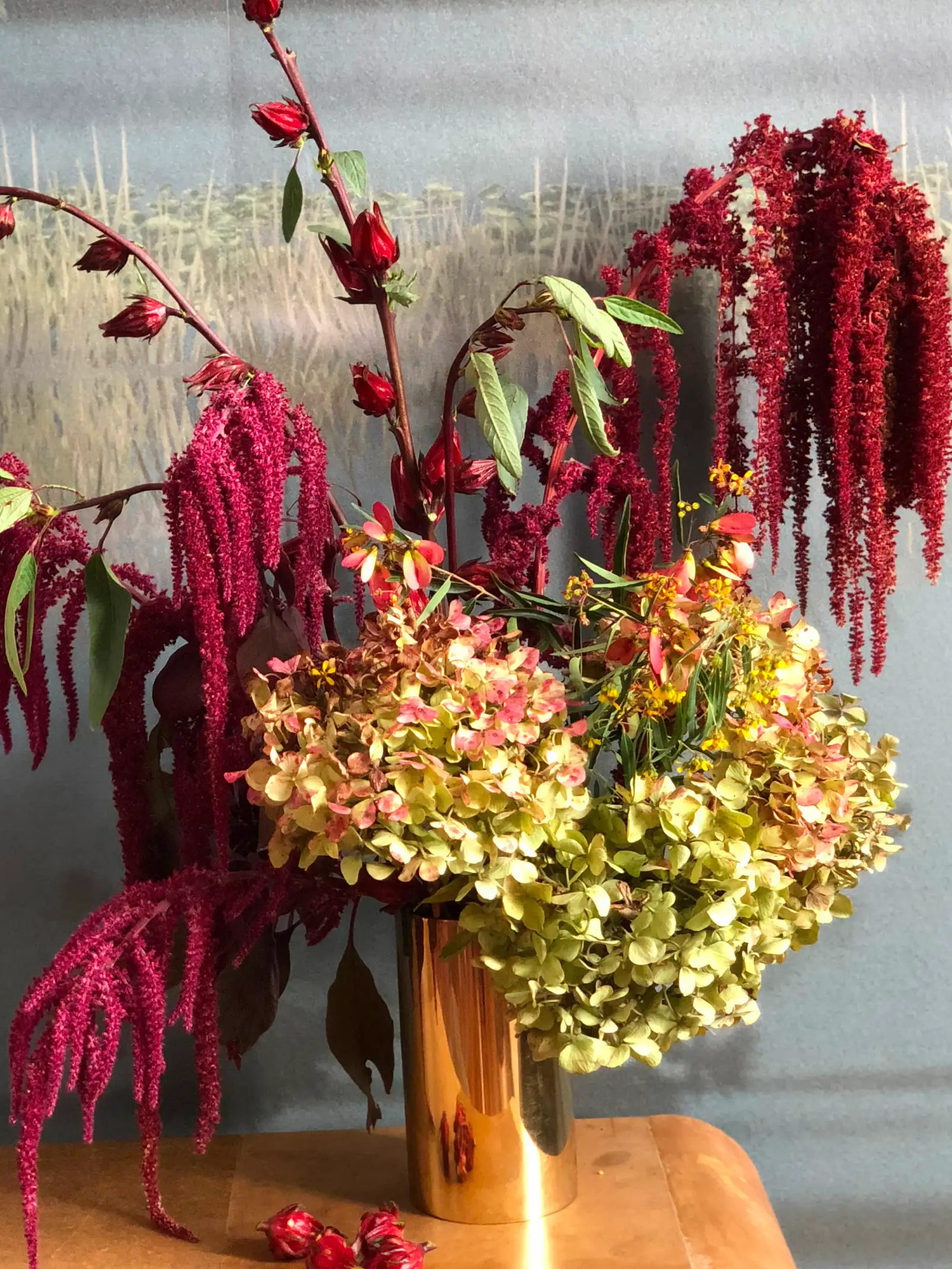 Arreglo floral con hortensias, amaranto y flores rojas en jarrón dorado para decoración elegante y naturalista.