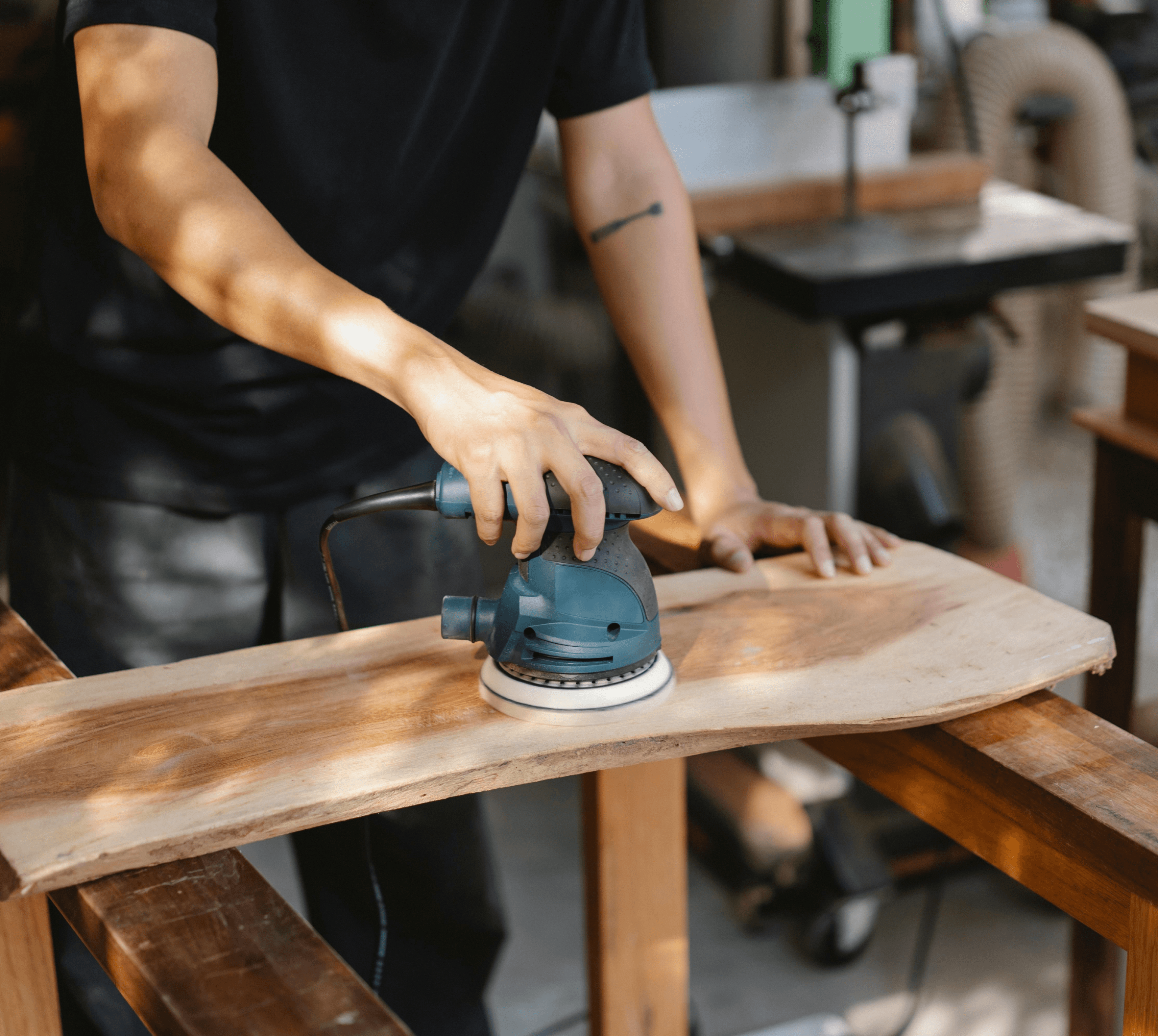 Un employé décape un meuble en bois à l'aide d'une ponceuse