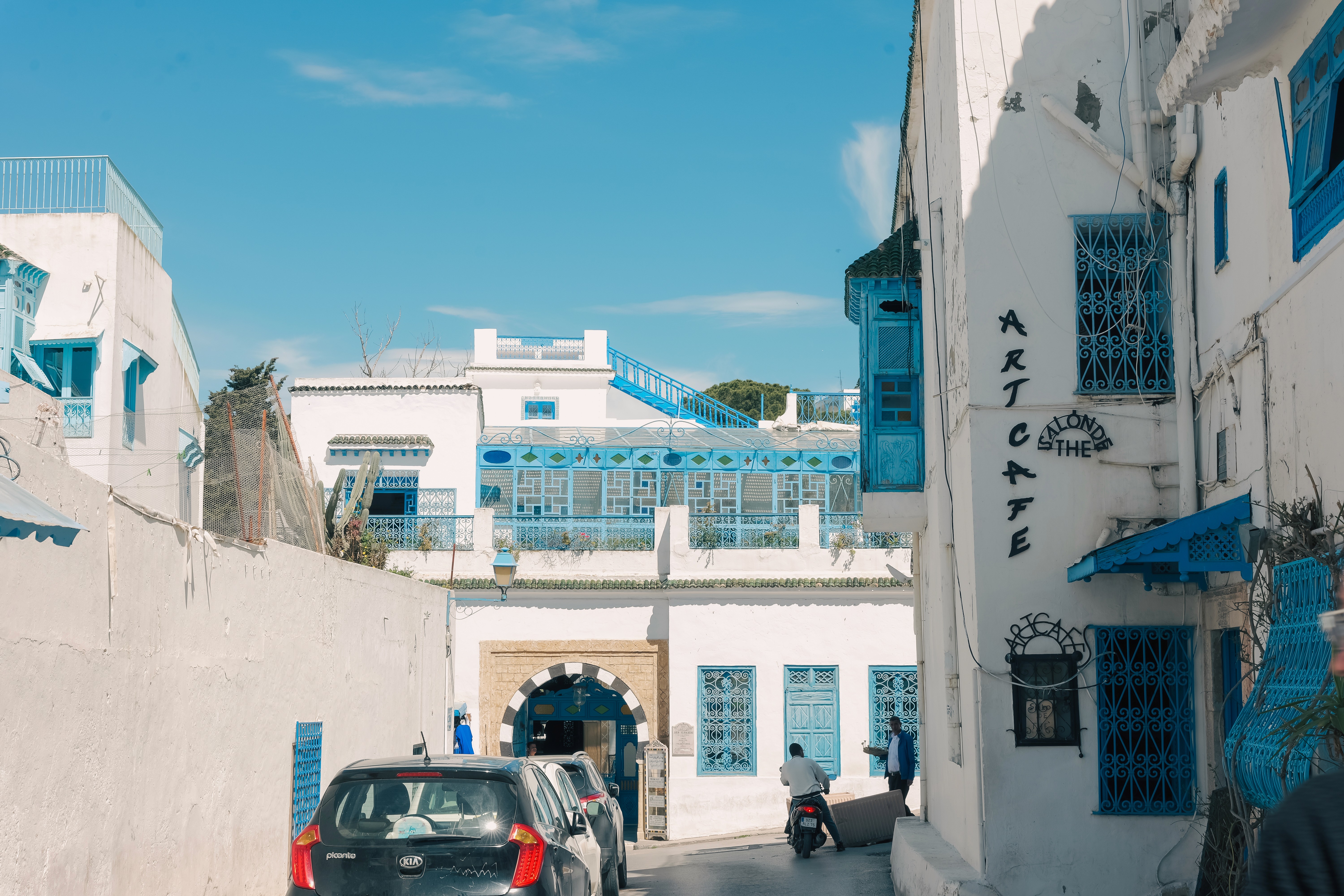 A red gondola car travels on cables over a green valley with a large lake and a town on its shore.