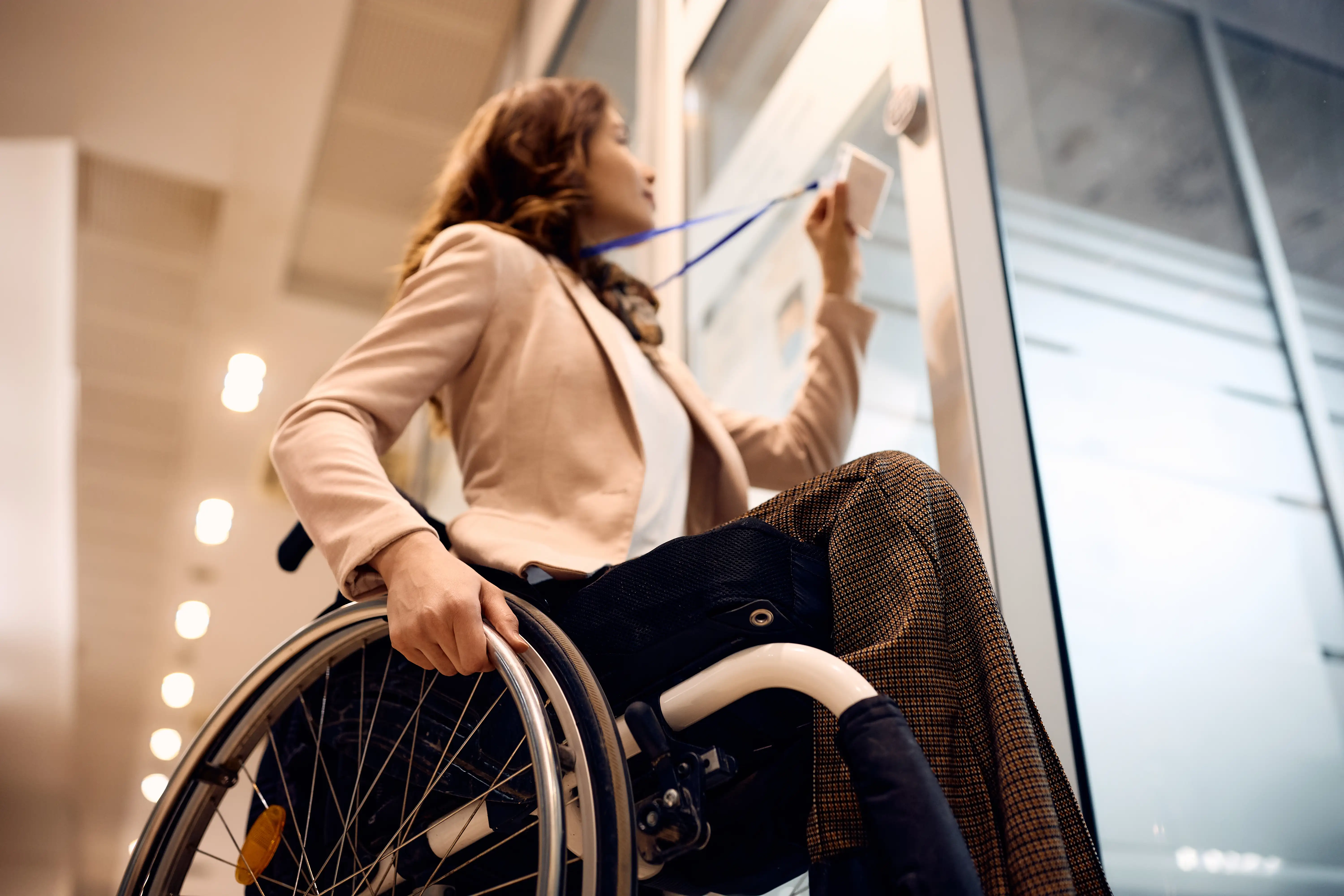 Professional woman using a wheelchair scanning an ID badge to enter an accessible office building, illustrating workplace accommodations under California law