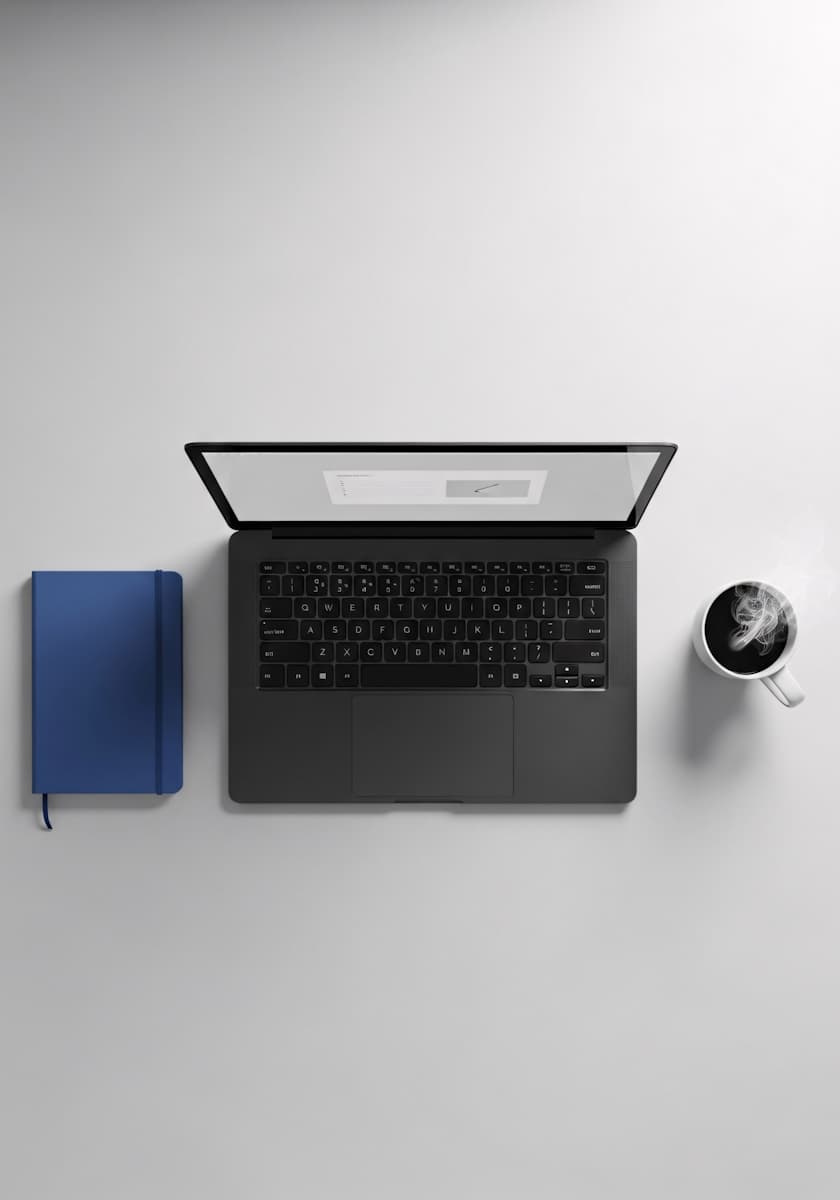 ein bild von einem Laptop, rechts ist ein kaffee, links ist ein blaues buch