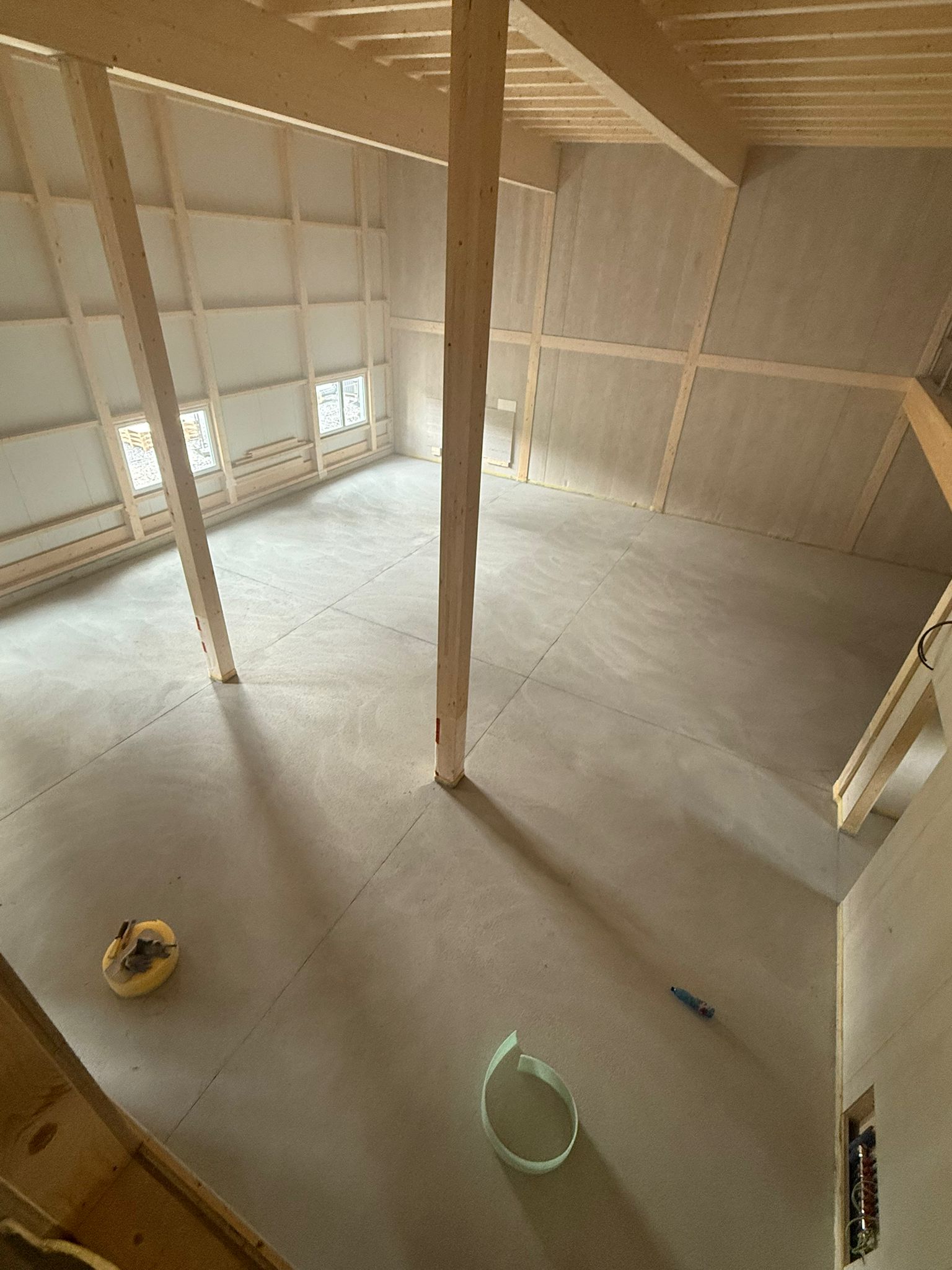 Innenansicht einer Baustelle. Holzbalken und unverputzte Wände vermitteln ein großzügiges Raumgefühl. Eine Rolle Klebeband und andere Werkzeuge liegen auf dem Boden.
