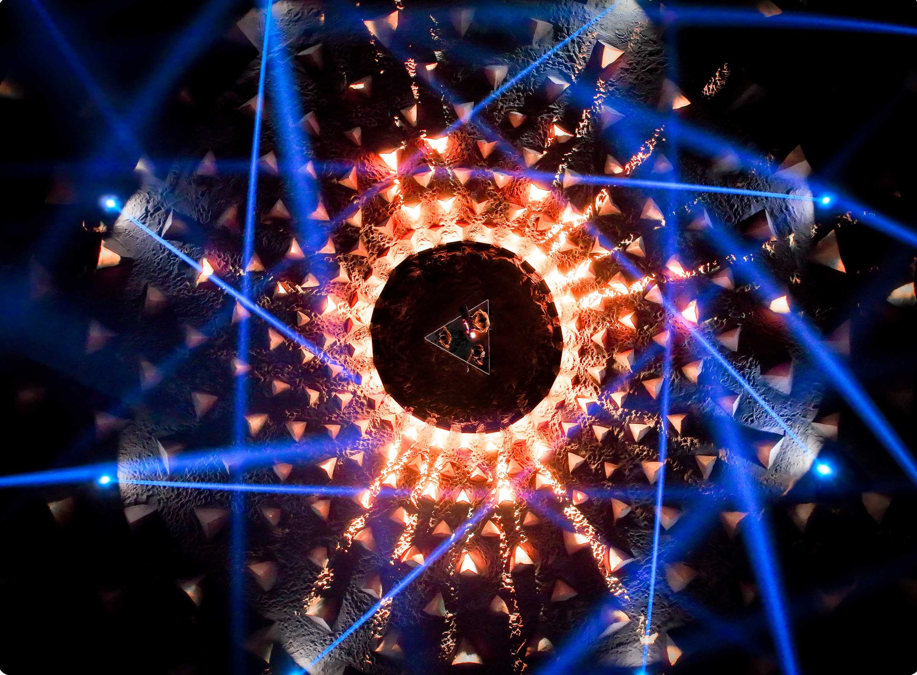 An epic light show over land art capturing the band ARIZONA performing on a triangular stage