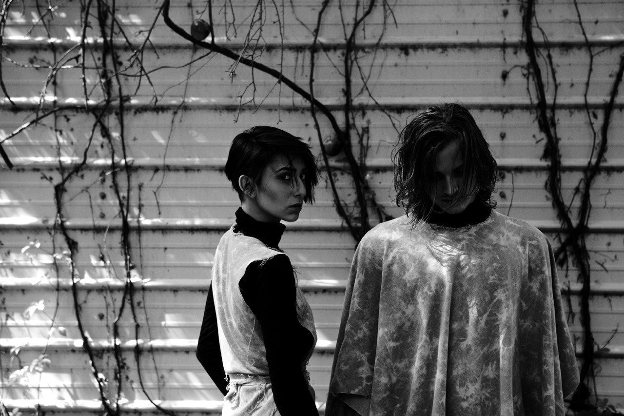 Black-and-white portrait of two models standing against a corrugated wall with vines, fashion editorial for Benjamin Jean.