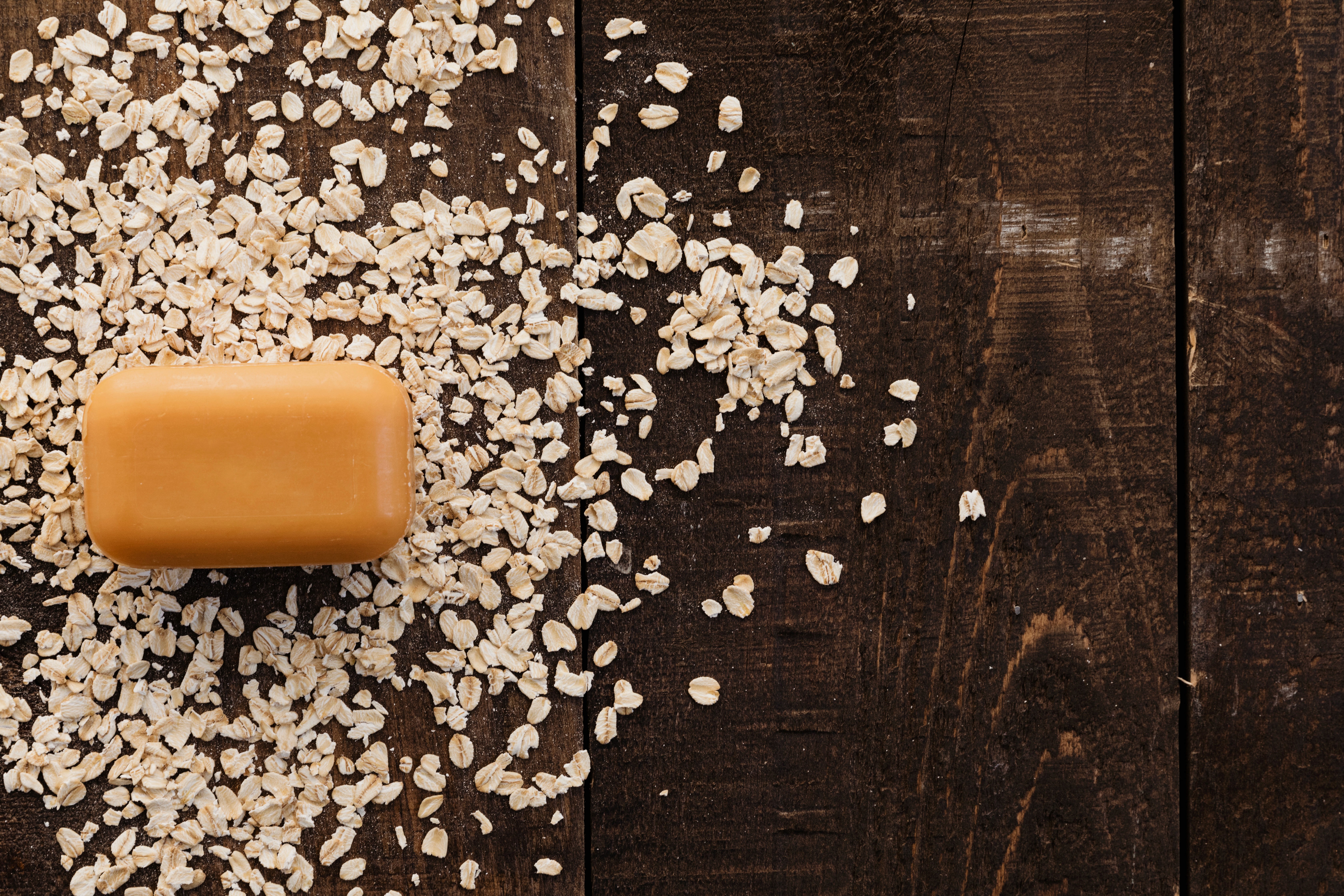 Oat soap bar surrounded by loose oats on dark wood