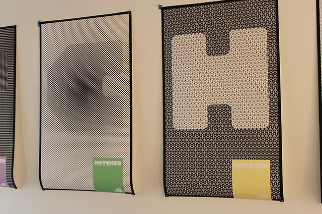 A set of black and white printed posters that show a letter and a colorful square near a corner with text Hatched.