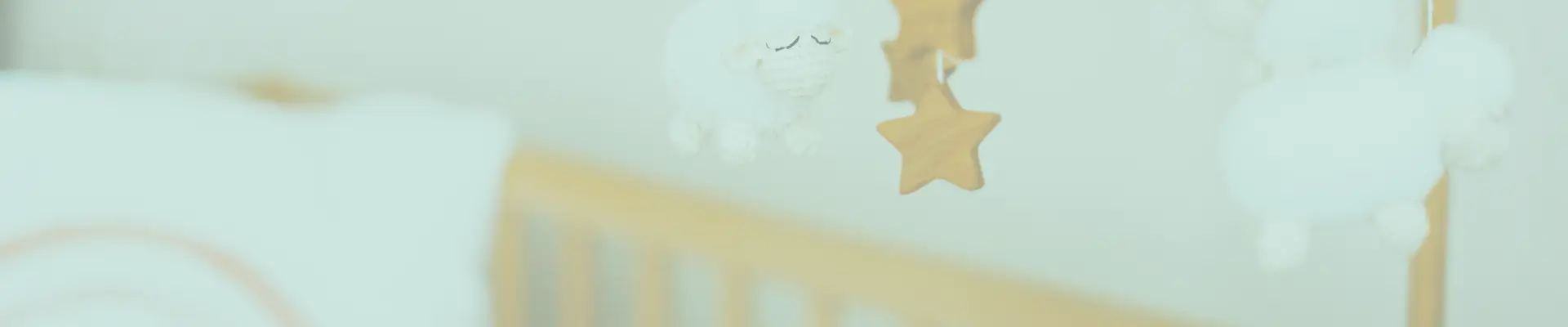 Close-up of a baby mobile hanging above a crib, featuring white plush sheep and wooden stars for soothing sleep.