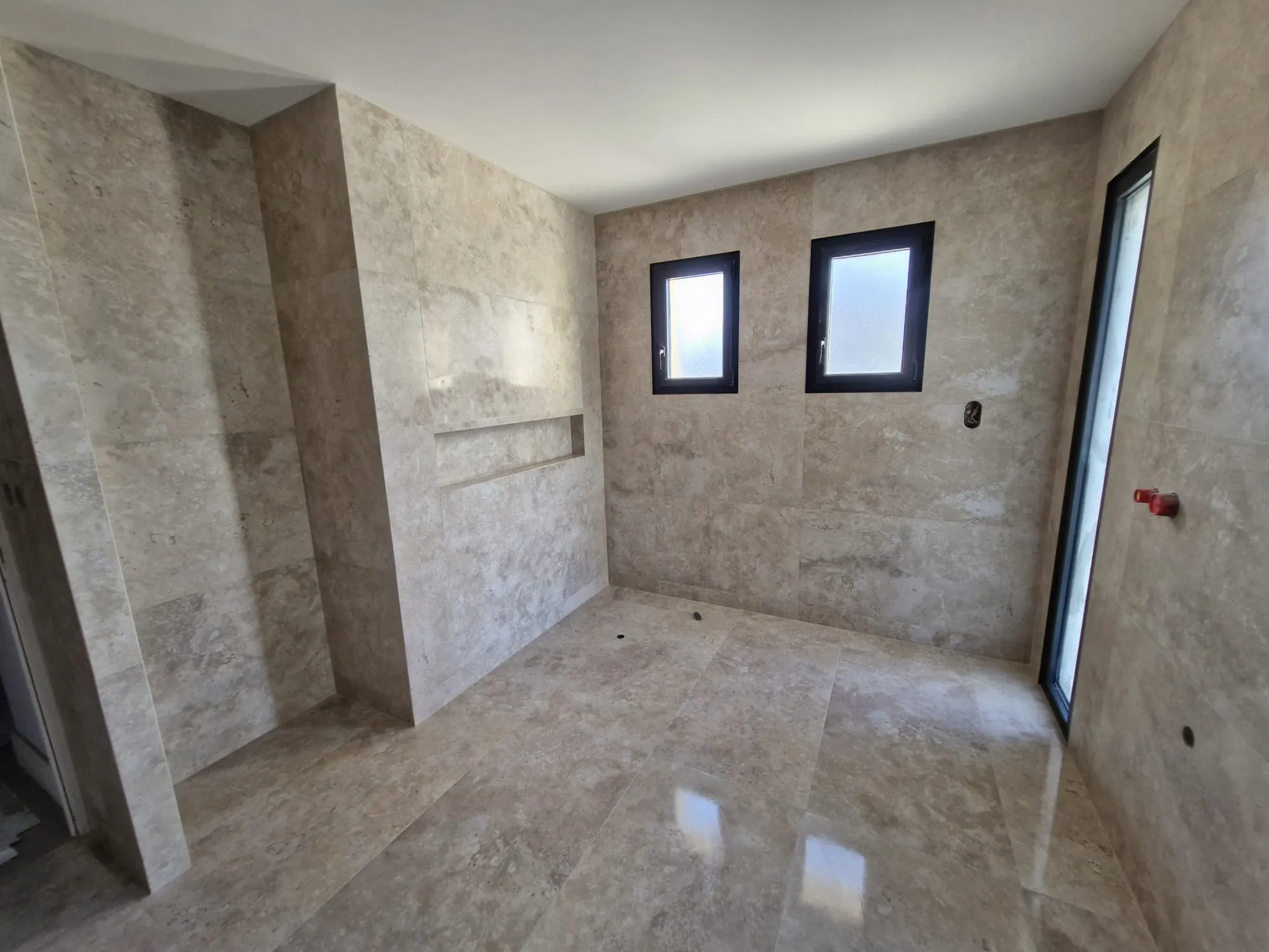 Salle de bain terminée : carrelage travertin au sol et au mur avec niche encastrée