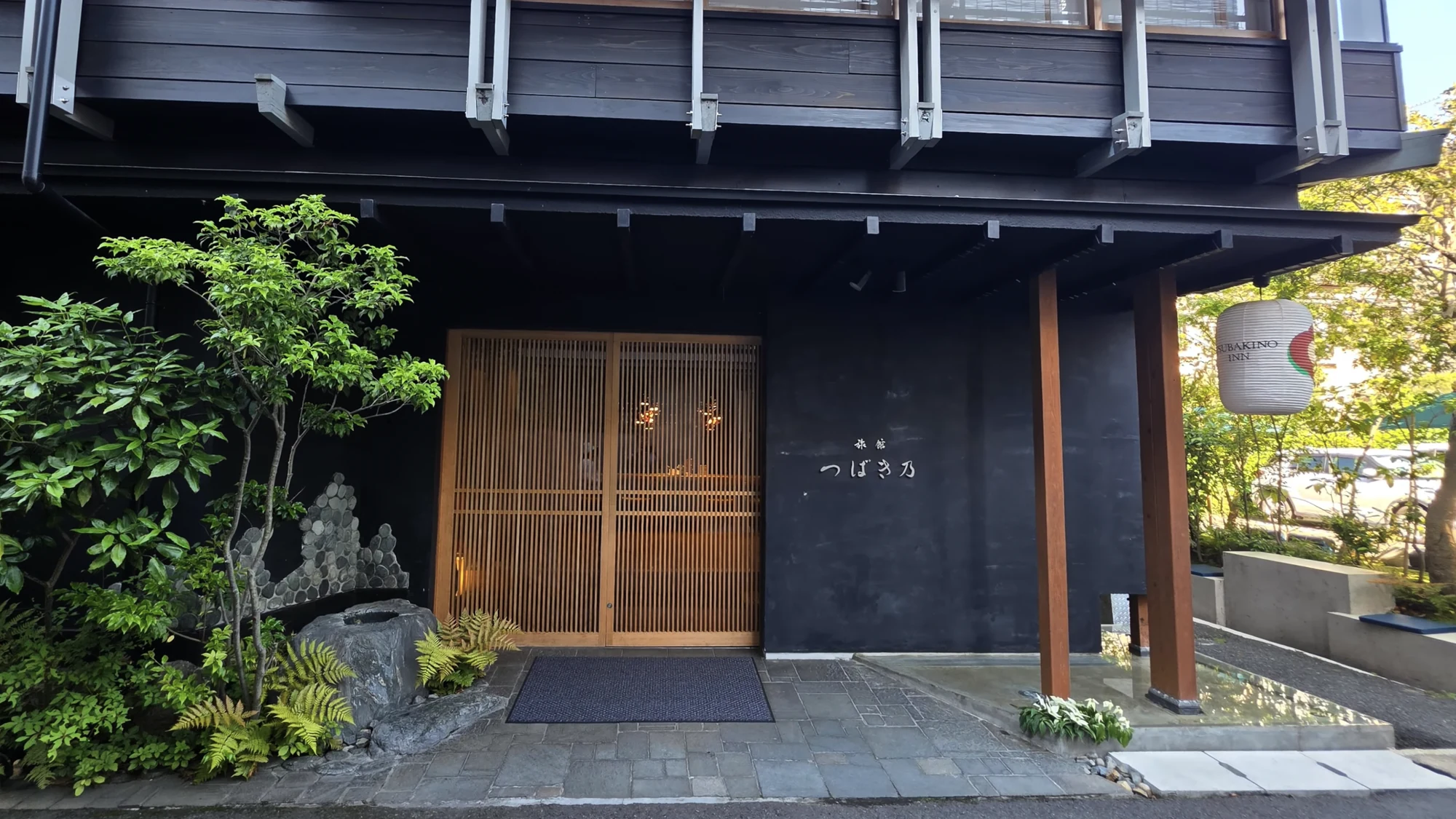 The dark timber entrance of a contemporary Kinosaki inn with a stone approach.