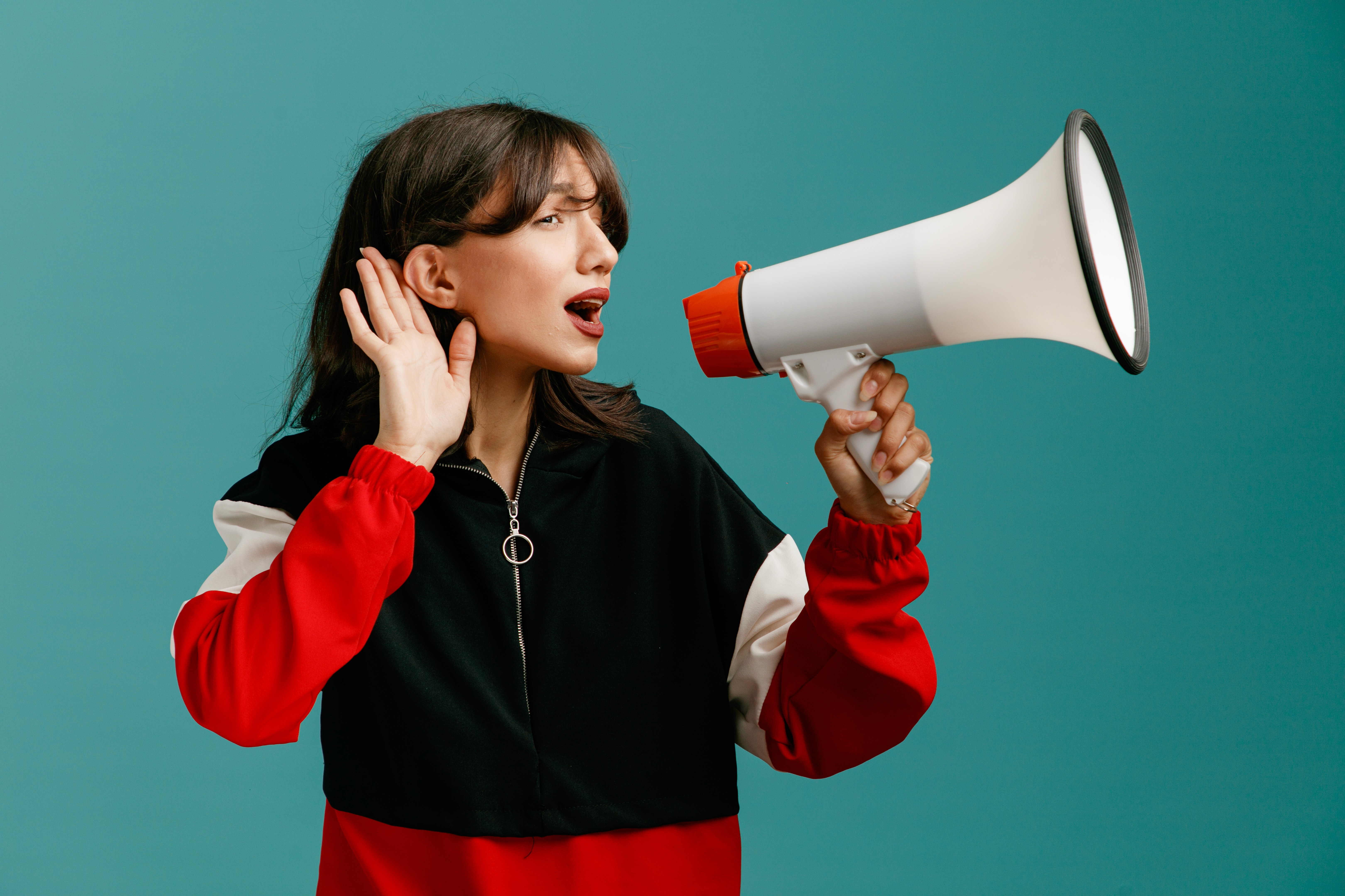 Femme utilisant un mégaphone et tendant l’oreille sur fond bleu, illustrant l’influence, la communication digitale, l’engagement des audiences et l’impact des réseaux sociaux.
