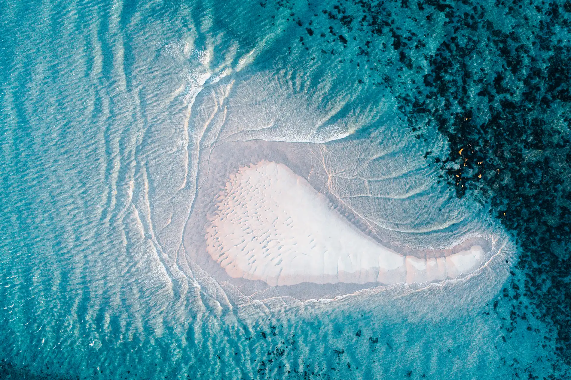 Aerial of a pale sandbank shaped by current in clear turquoise water