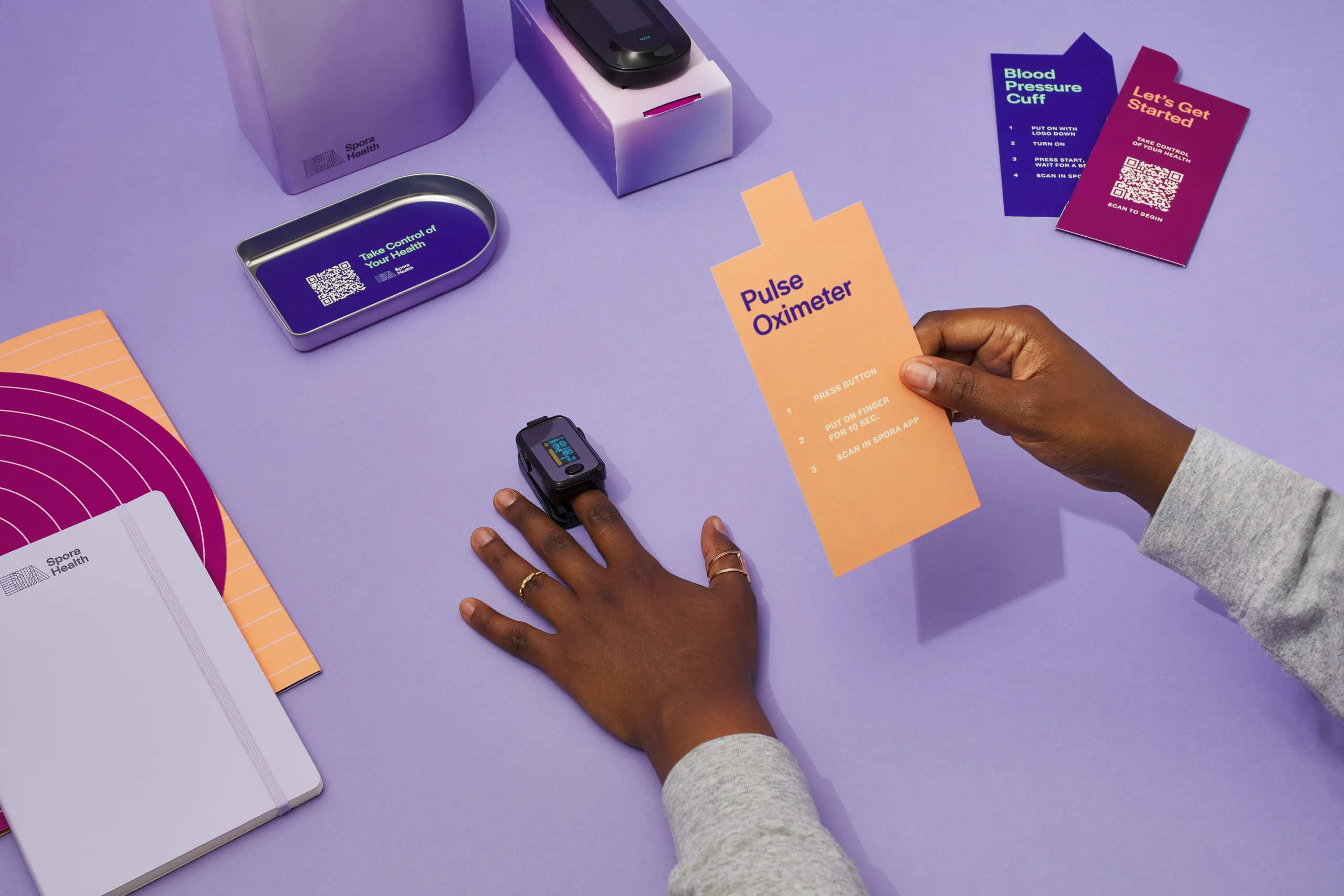 Person using a fingertip pulse oximeter alongside Spora Health Momma’s Kit instructions and health monitoring tools