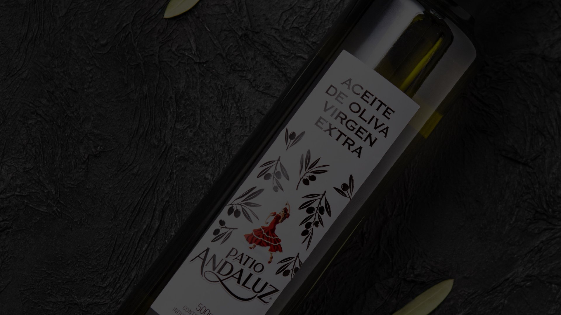 A bottle of Patio Andaluz extra virgin olive oil on a dark textured background. The label features leaf designs and a red figure, evoking elegance.