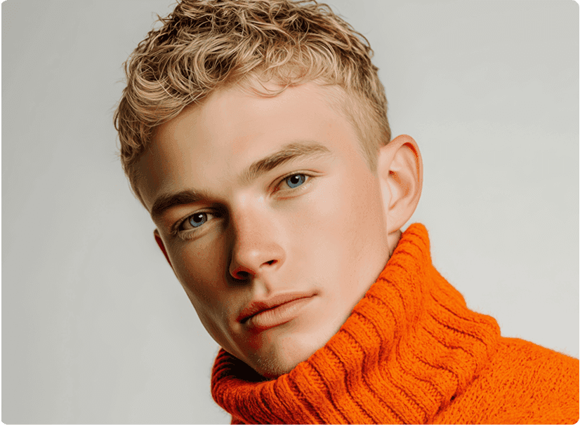 A young person with short blond hair gazes confidently at the camera while wearing an eye-catching bright orange turtleneck sweater.