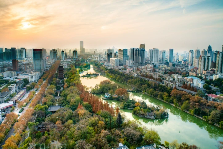 Elegant stone building facade with French balcony windows and a wide entrance framed by glass panels, viewed on a rainy street with reflections on the wet pavement.