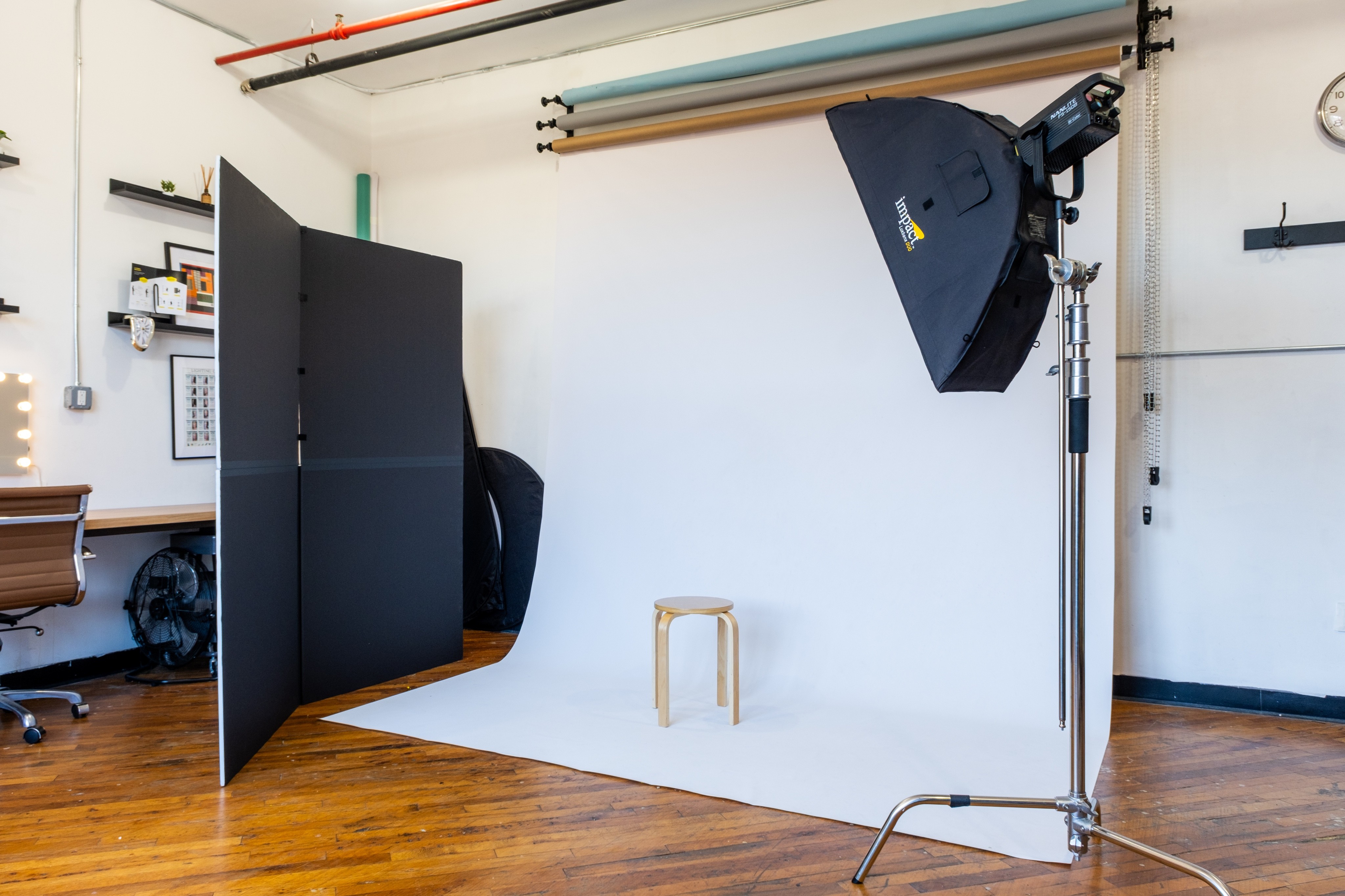 Close-up of a professional Amaran 100x studio light, with additional lighting equipment in the background against colorful backdrop rolls in a photo studio.