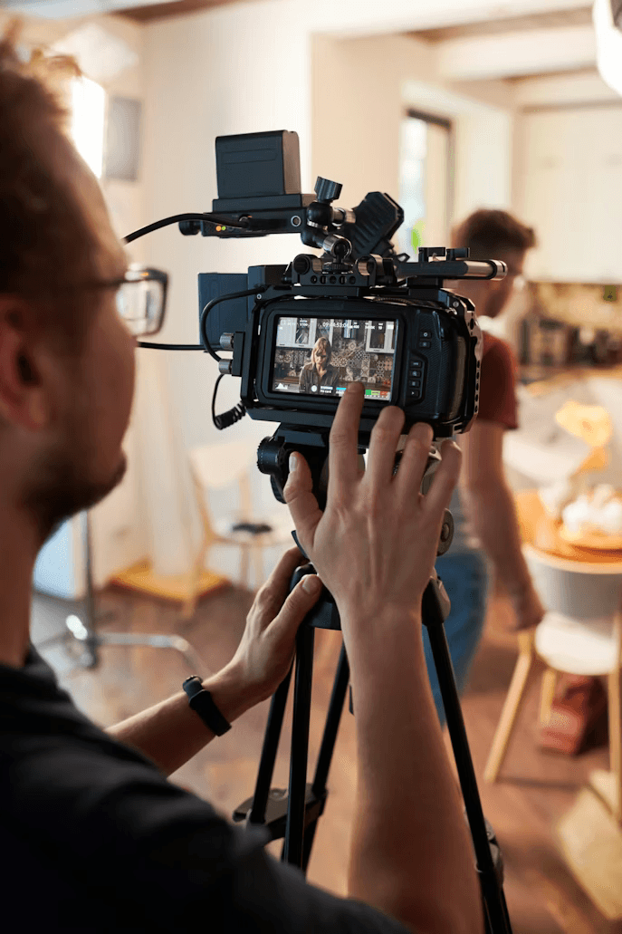 Close-up portrait of a person wearing a gray insulated hooded jacket with the hood up, showing their face framed by the hood against a light background.