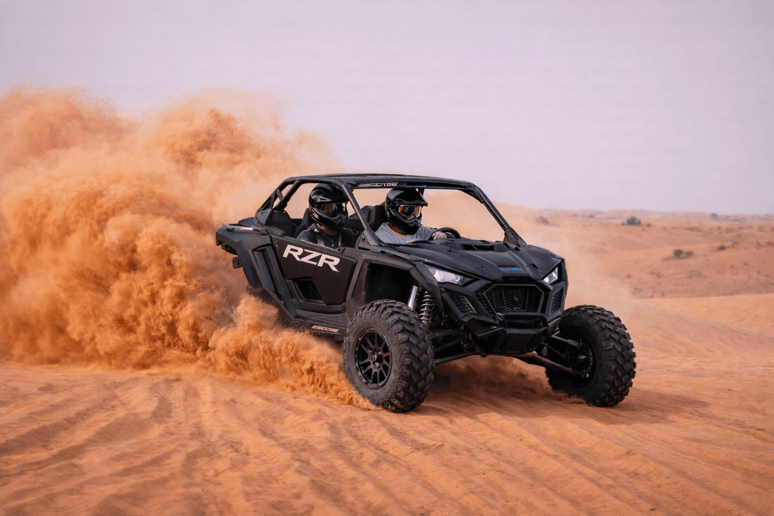 Two people riding a Polaris RZR 2-seater dune buggy during a desert buggy tour in Dubai