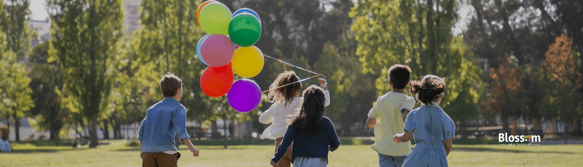 Autistic children running across a grassy field, holding balloons, with tall trees outdoors in GA.