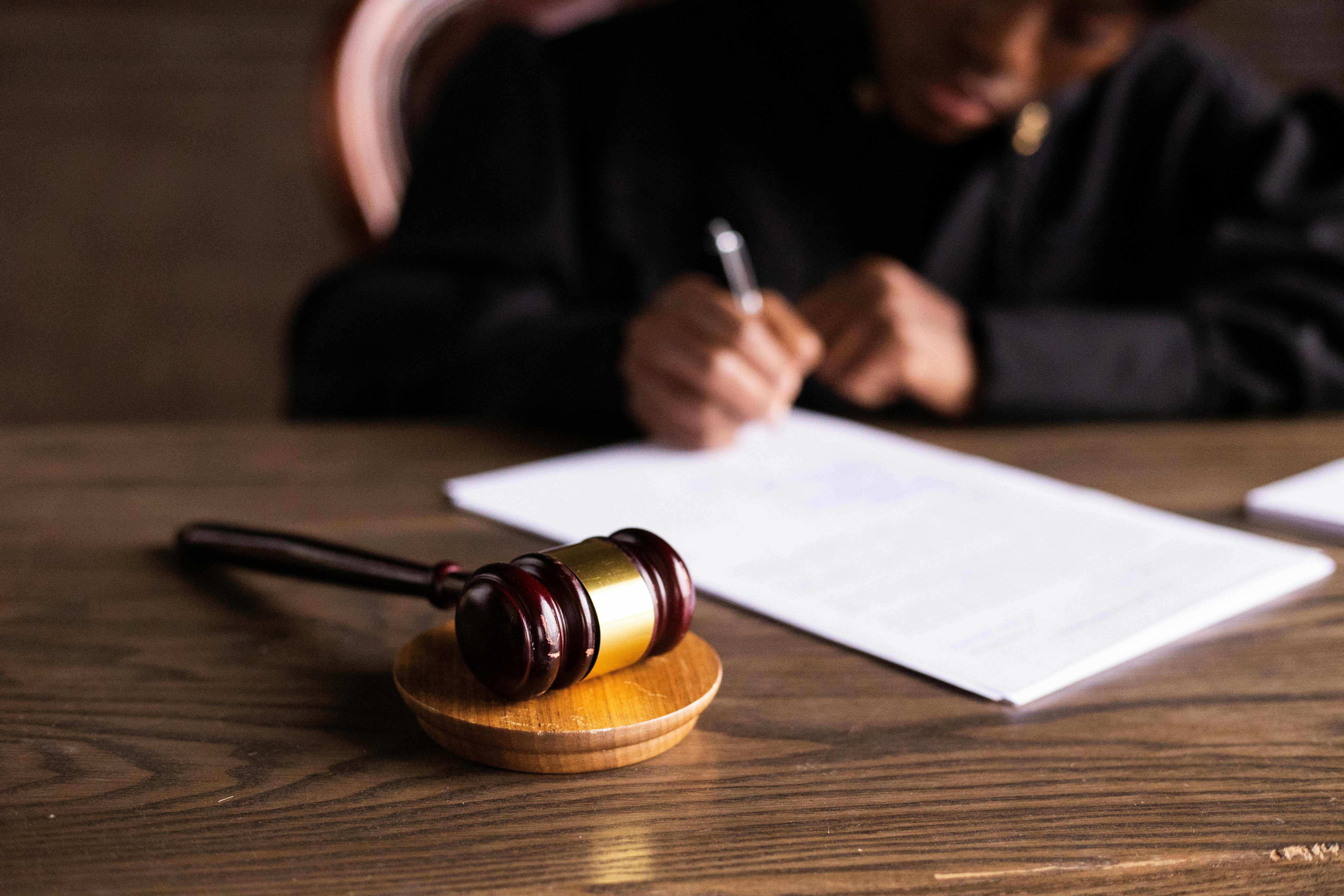 A gavel on a courtroom desk with a judge filling out a piece of paper