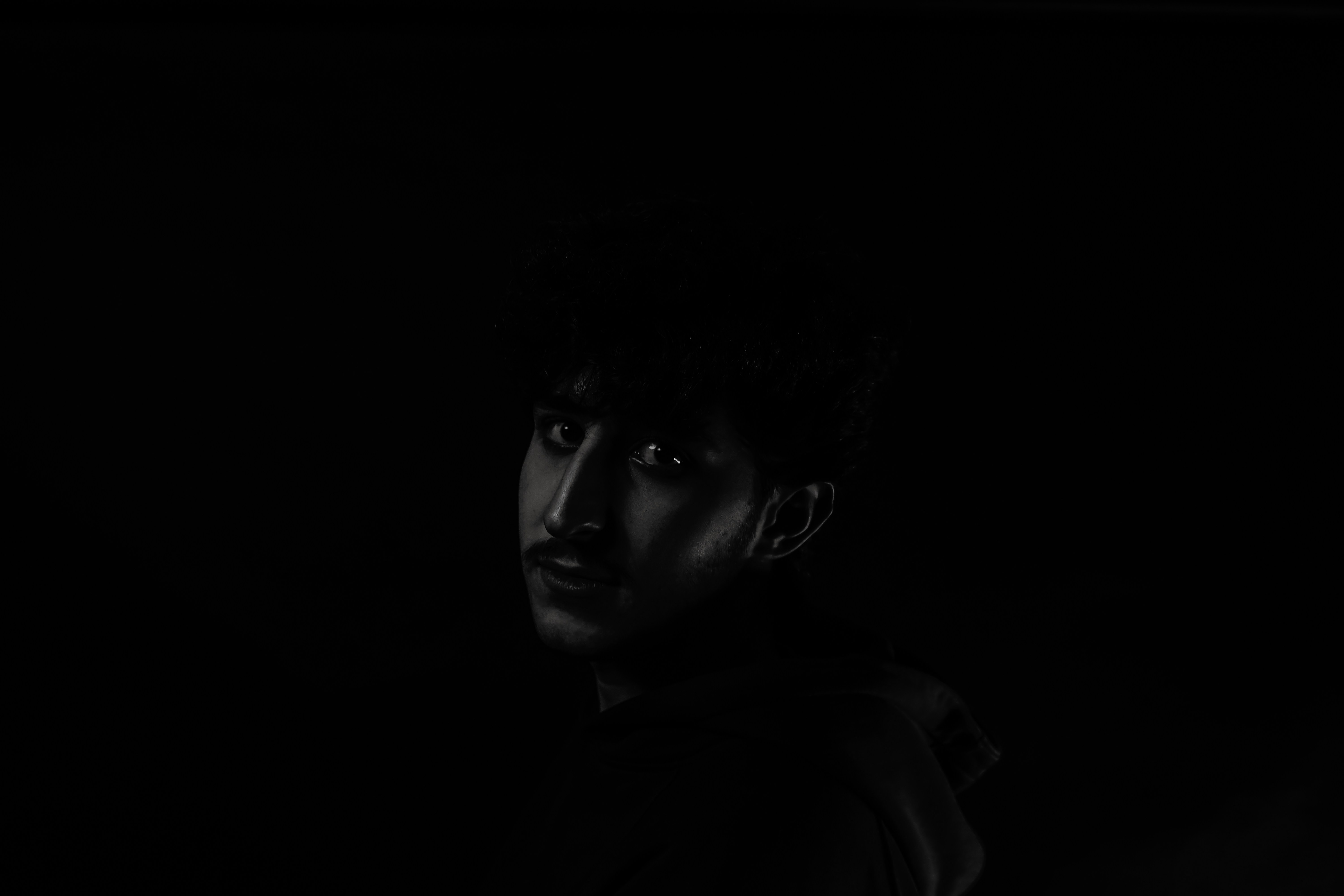 A man standing in the dark with his head turned to the side