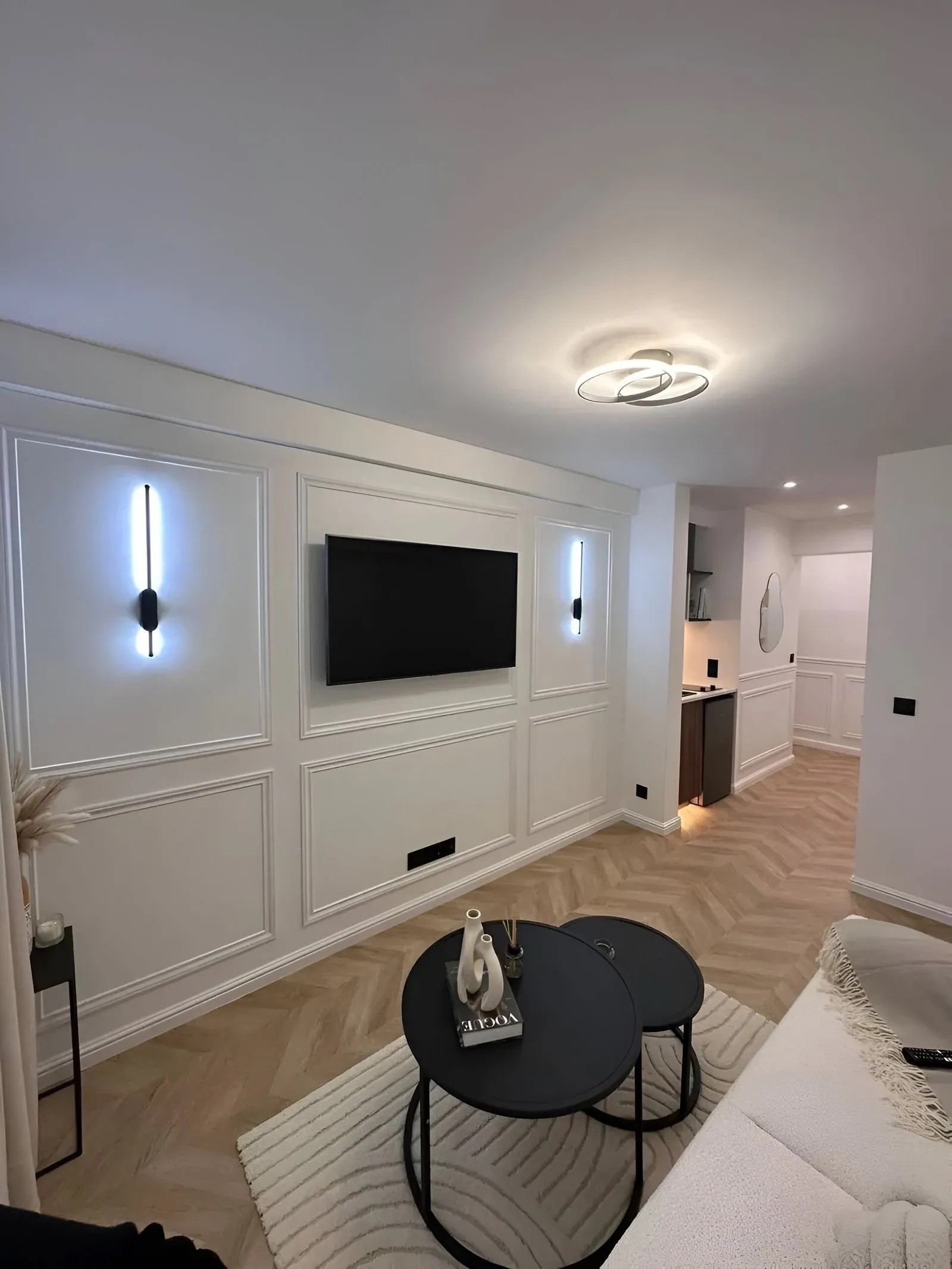 Détail du mur TV avec moulures décoratives blanches et éclairage d'ambiance par appliques LED verticales bleues.