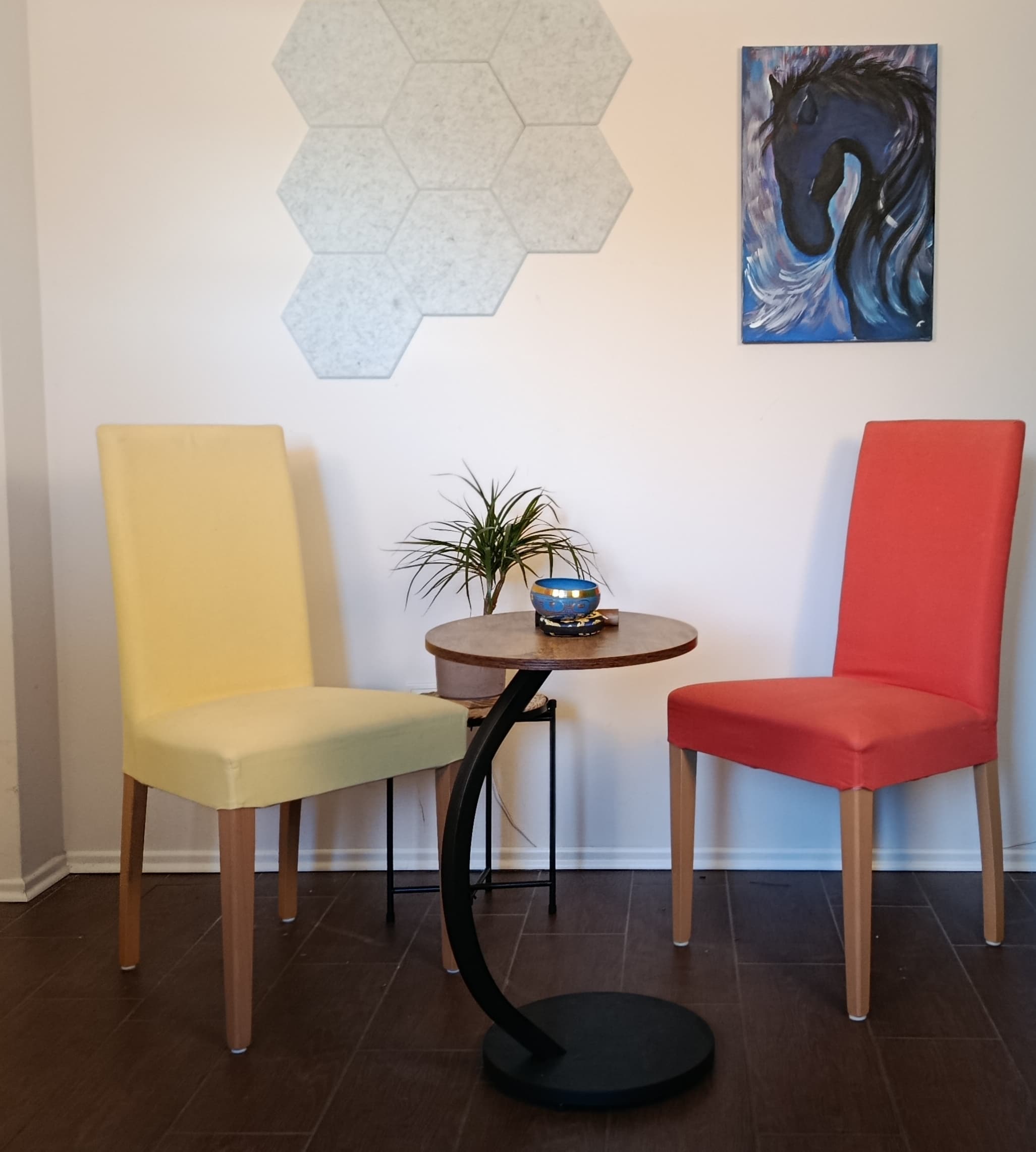 Gemütliche Sitzecke mit gelbem und rotem Stuhl, kleinem Tisch und Kunstwerken. Moderne Wohnraumgestaltung.