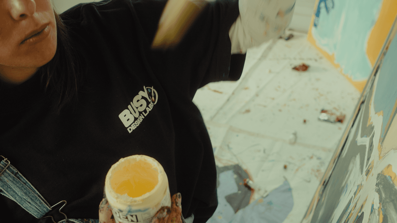 A person holding a cup of coffee while working on a large painting, focusing on adding fine details