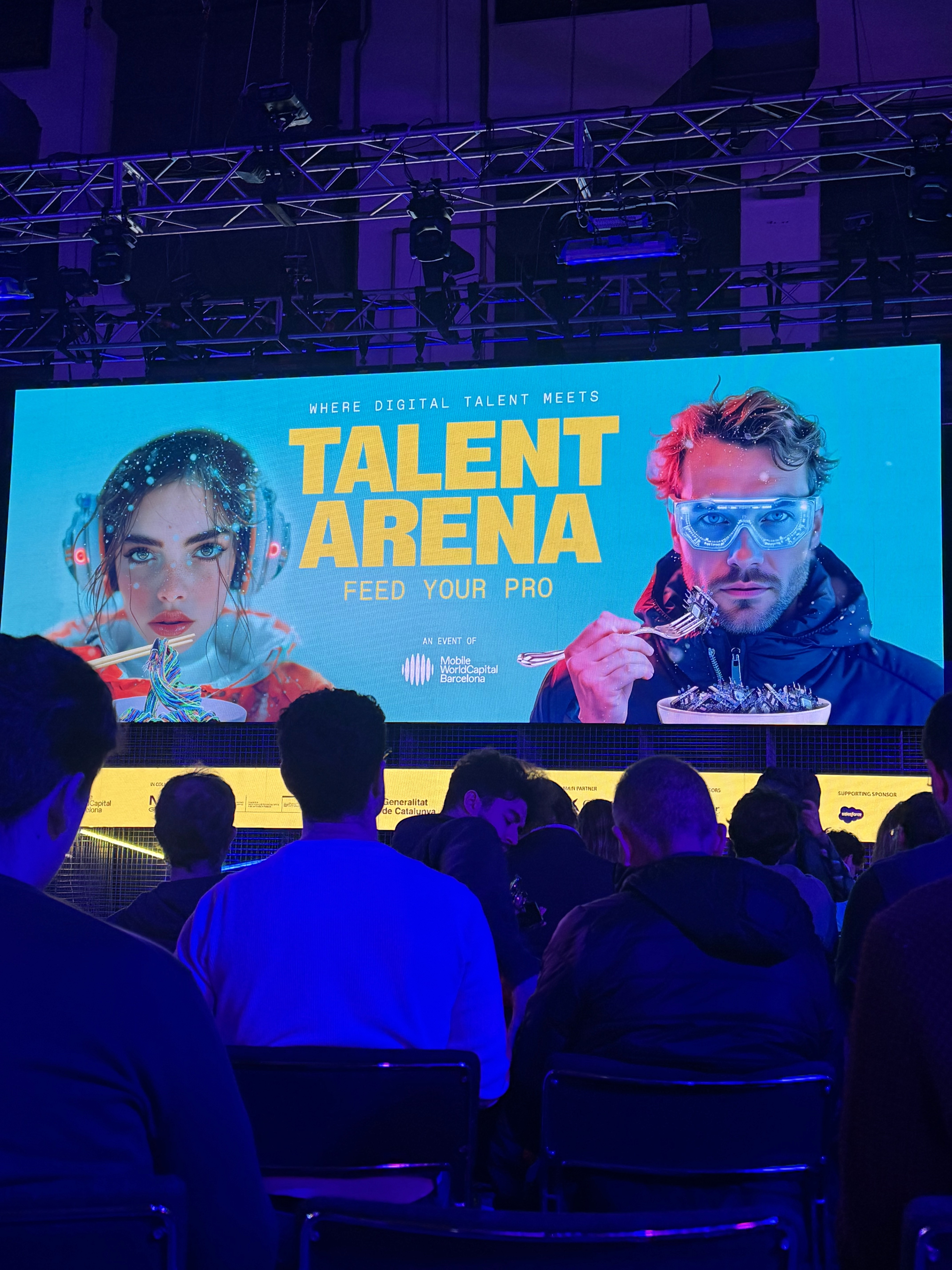 Audience seated in front of large “Talent Arena” stage screen at a tech or career event, featuring vibrant visuals of two speakers