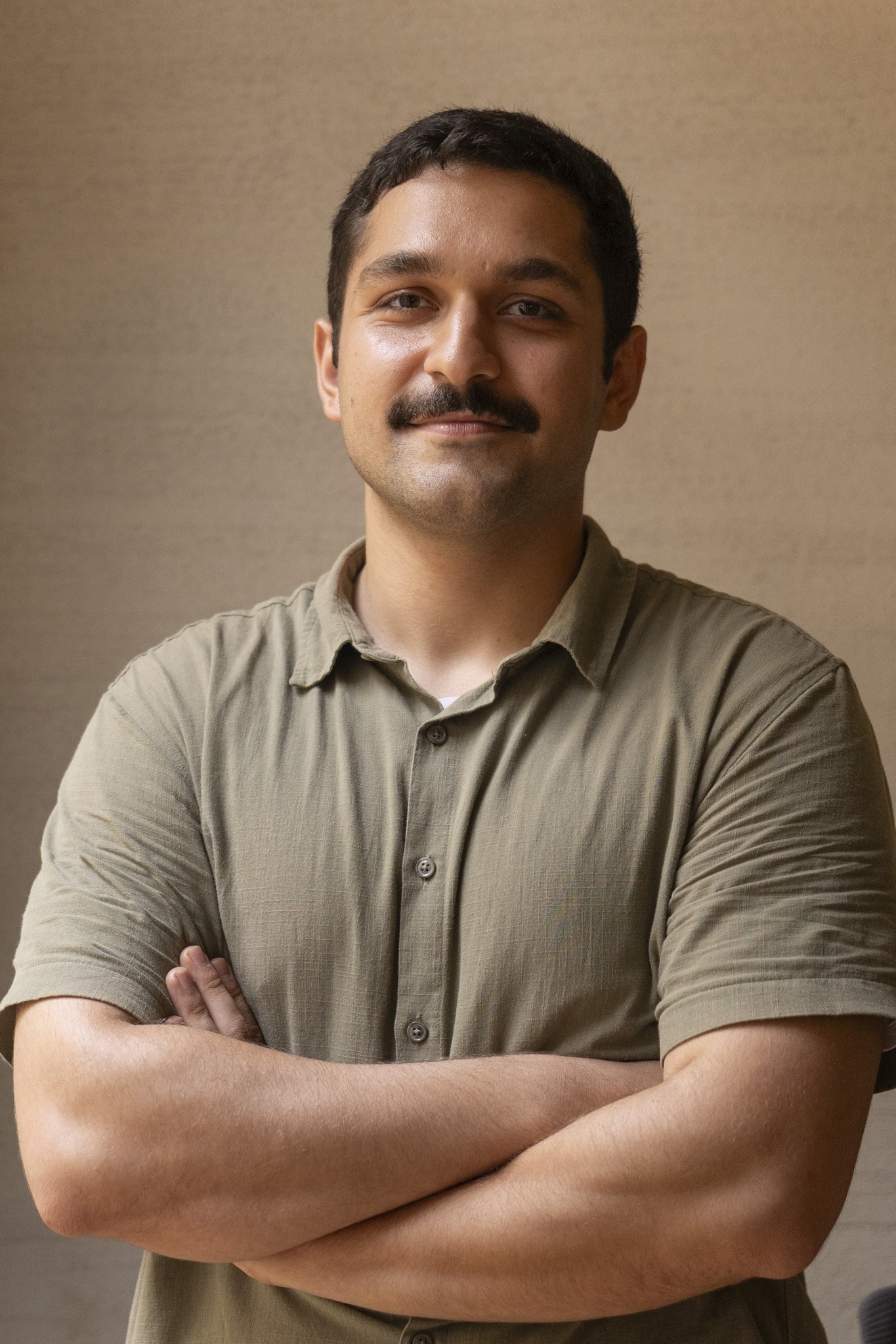 Portrait of a startup founder with arms crossed, wearing an olive shirt against a neutral background.