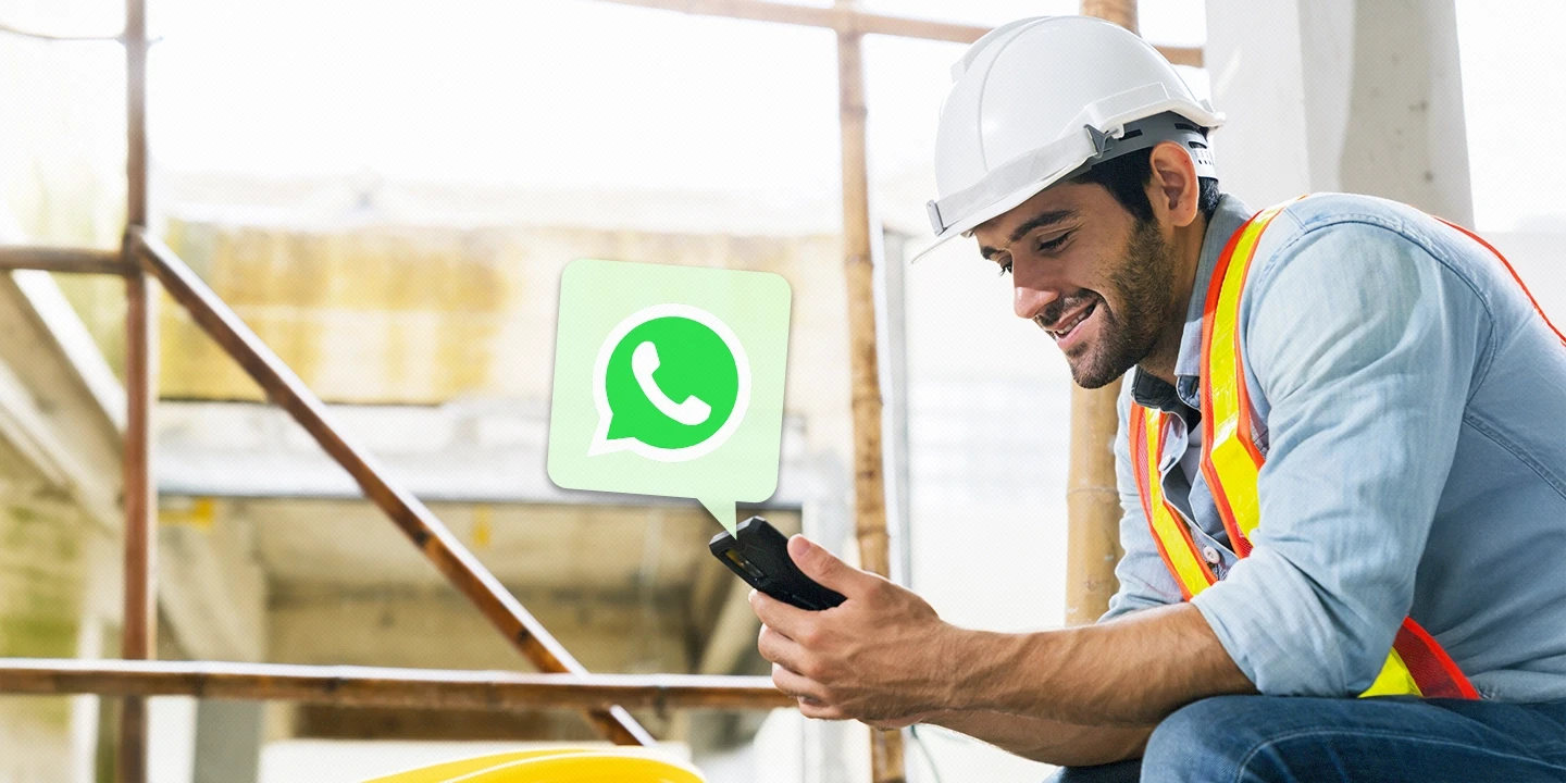 Trabalhador da construção civil usando capacete e colete refletivo, sorrindo enquanto se comunica pelo WhatsApp no celular