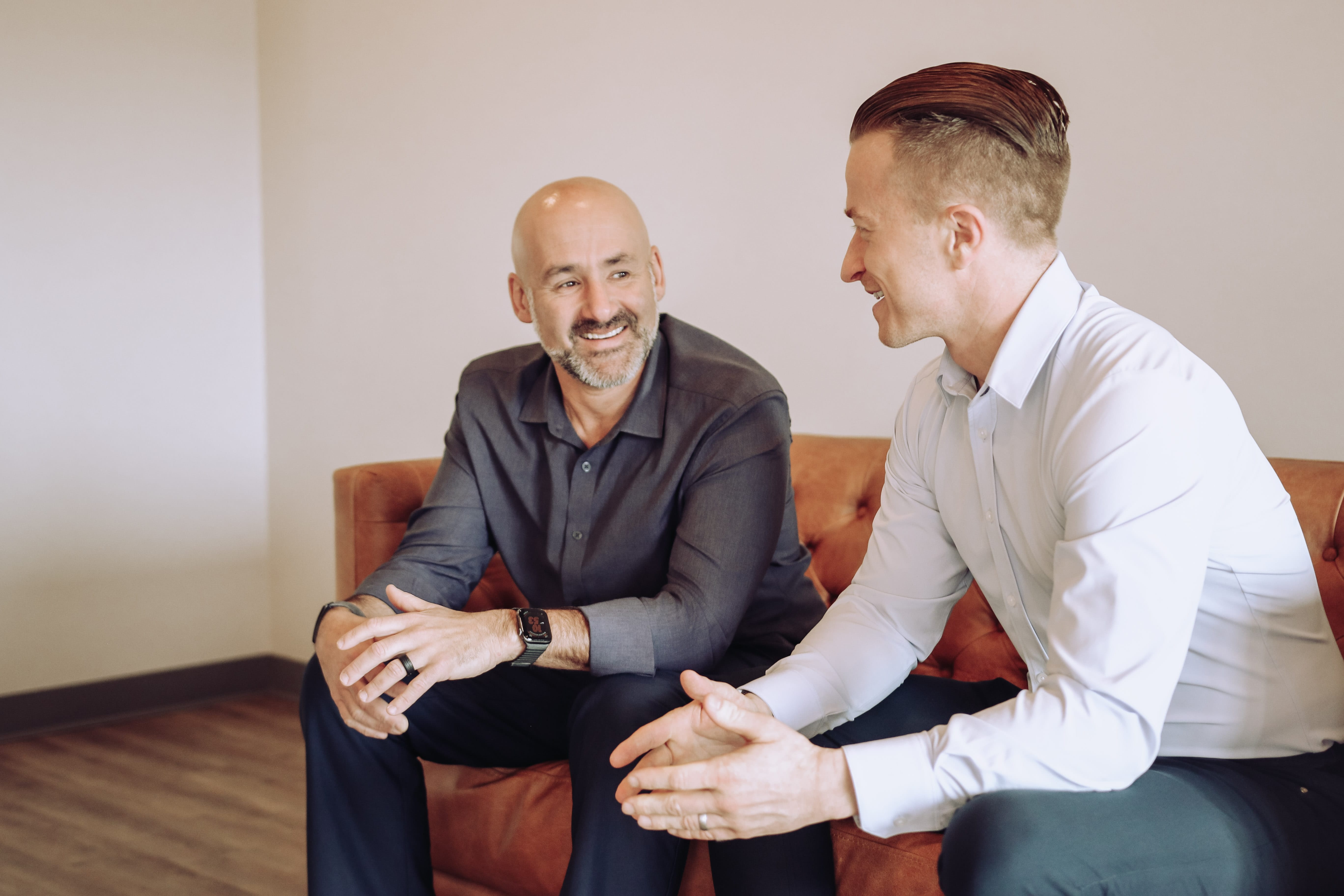 Two Premier doctors sitting on a couch in the office, smiling at each other in conversation.