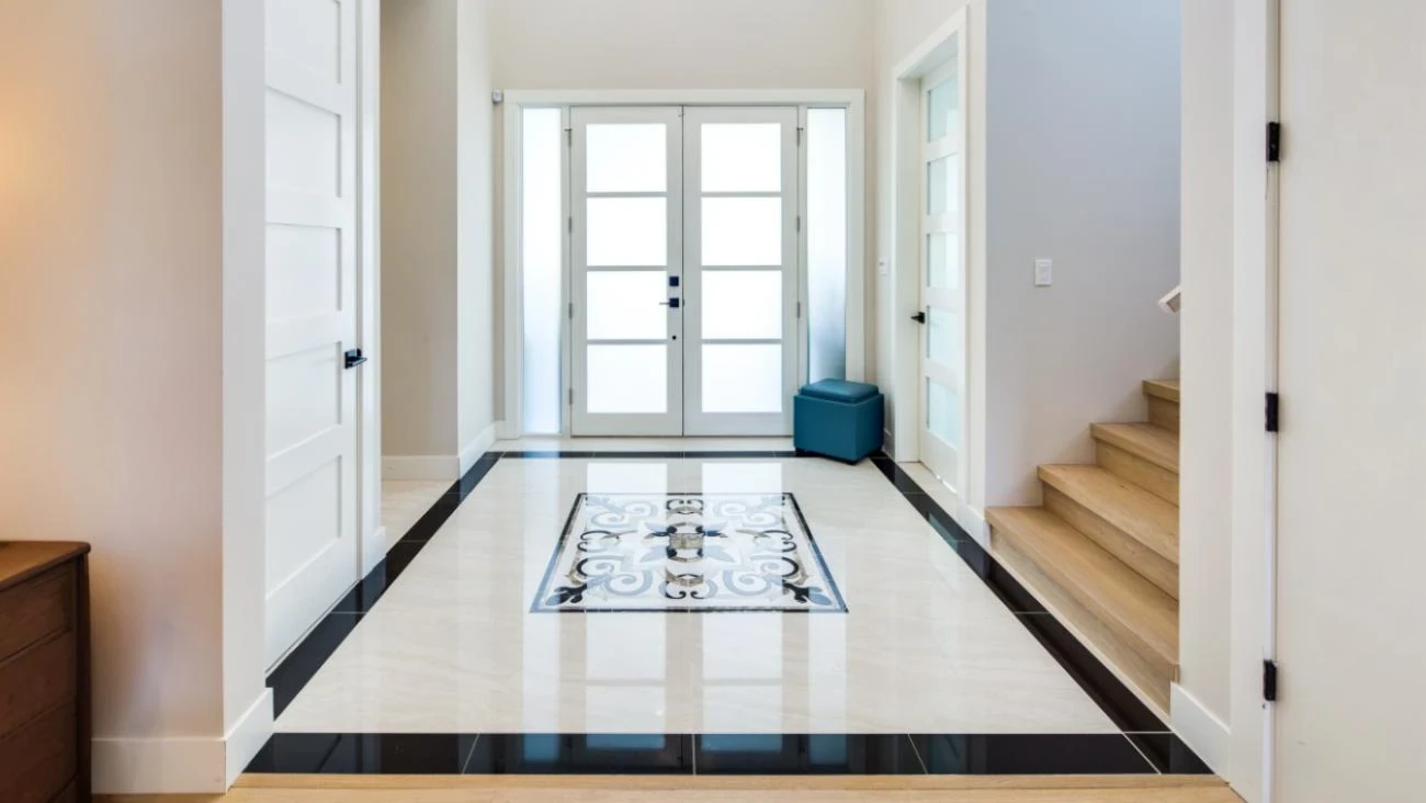 Luxury home entryway with decorative patterned tile inlay, black border trim, glass French doors, and contemporary staircase