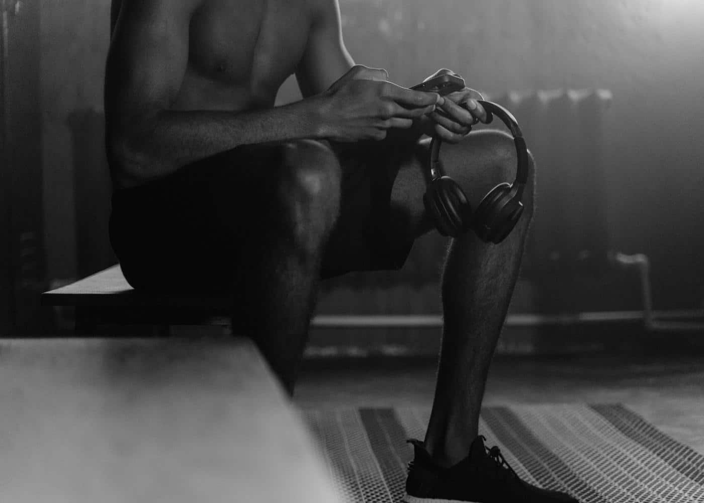 Man sitting down holding heatphones in one hand and looking at phone in the other