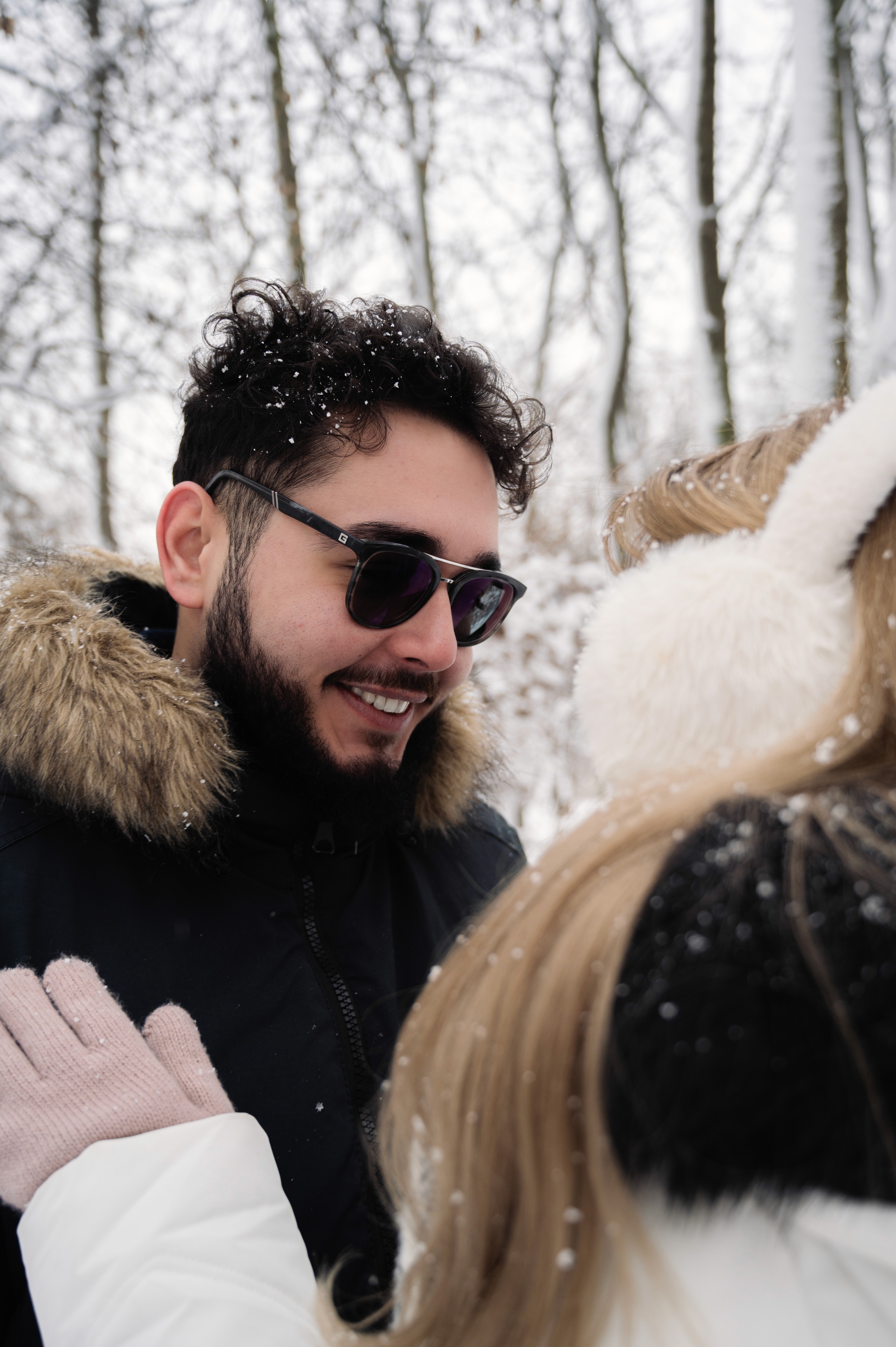 Cuplu zâmbind într-o ședință foto Save the Date de iarnă, realizată în lumină naturală, într-un parc acoperit de zăpadă